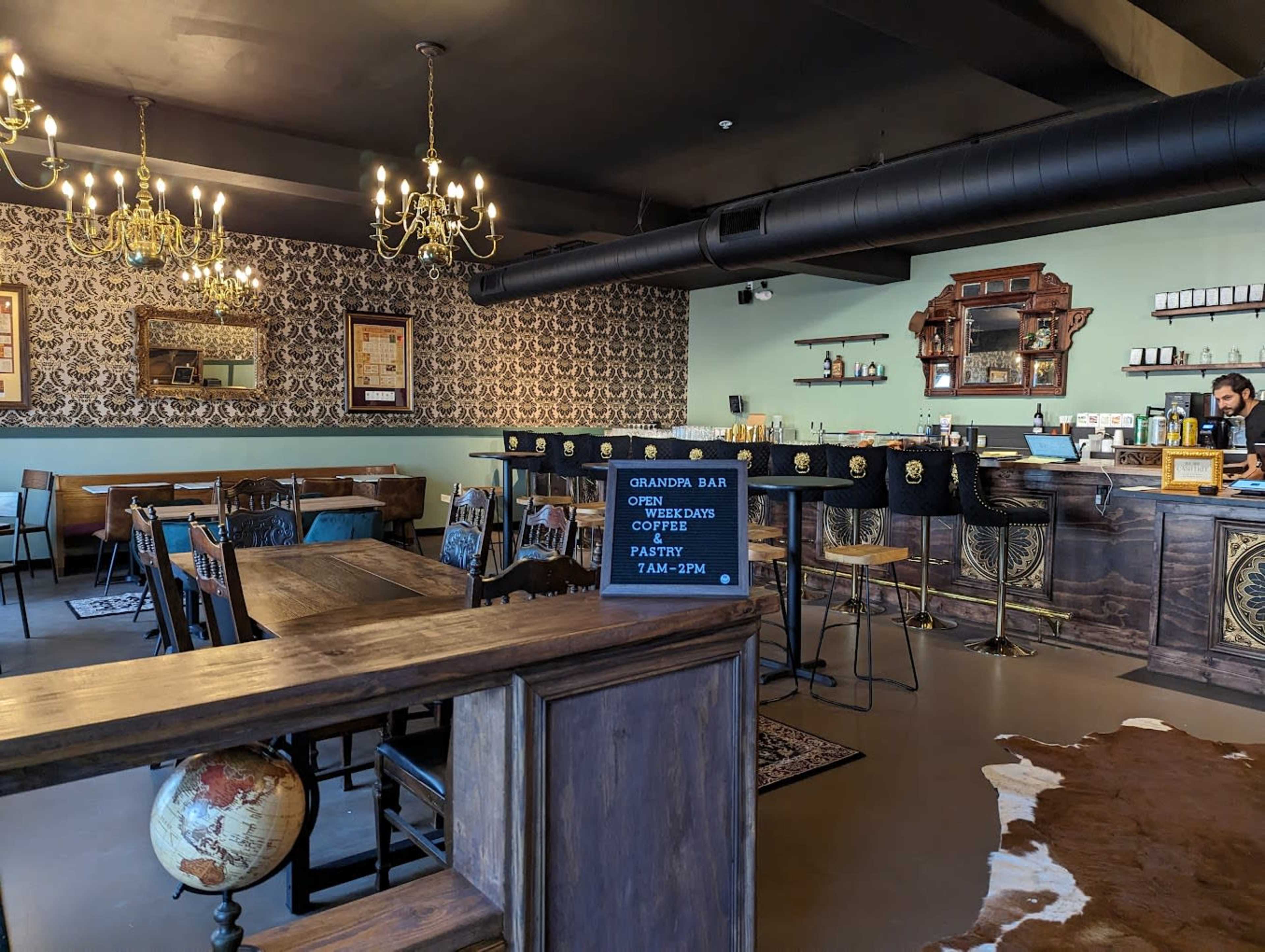 The image shows an interior of a café with wooden furniture, vintage décor, and a bar area, featuring a sign indicating operating hours.