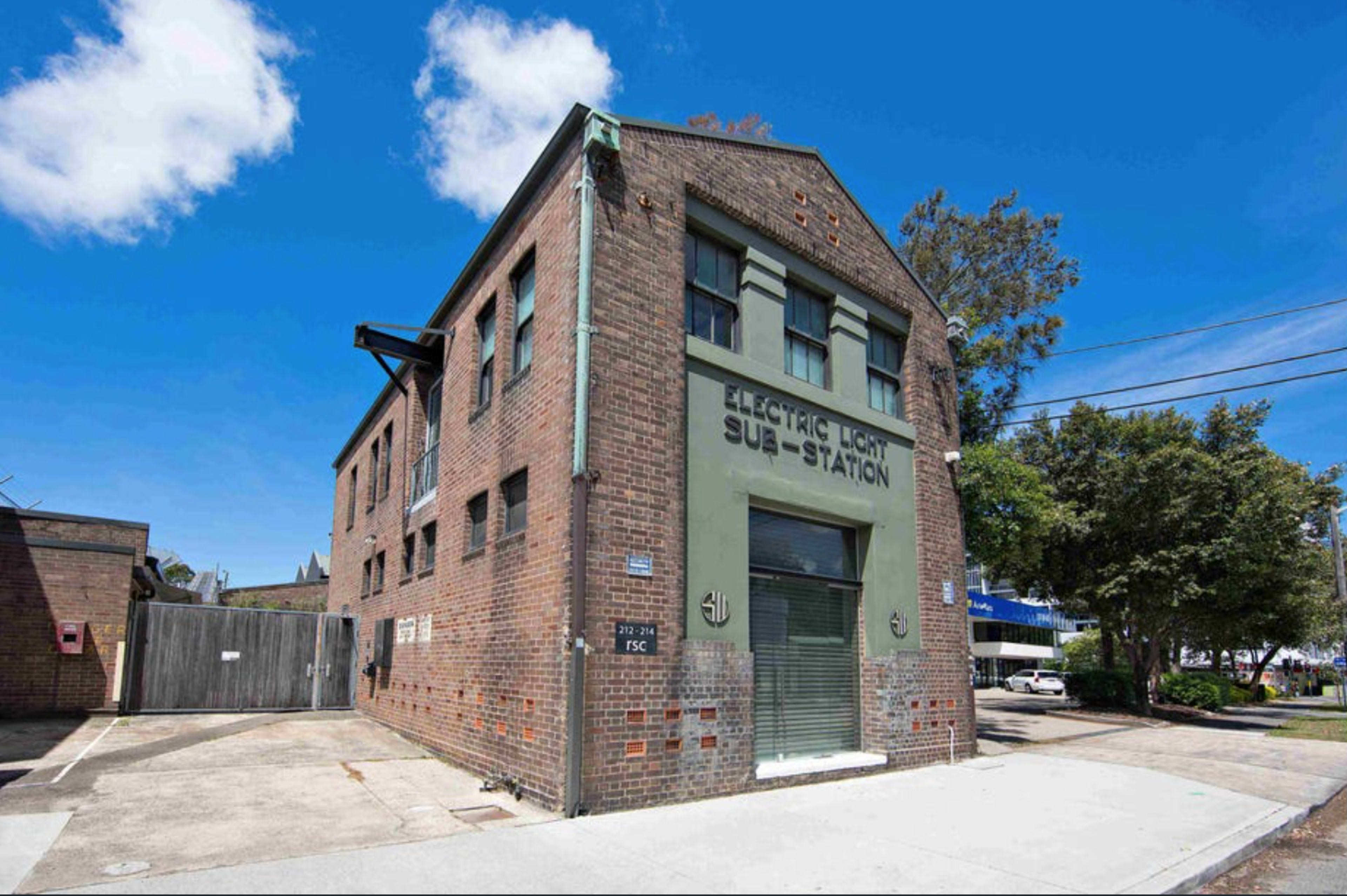 A two-story brick building labeled "ELECTRIC LIGHT SUB-STATION," with green detailing and a clear blue sky overhead.