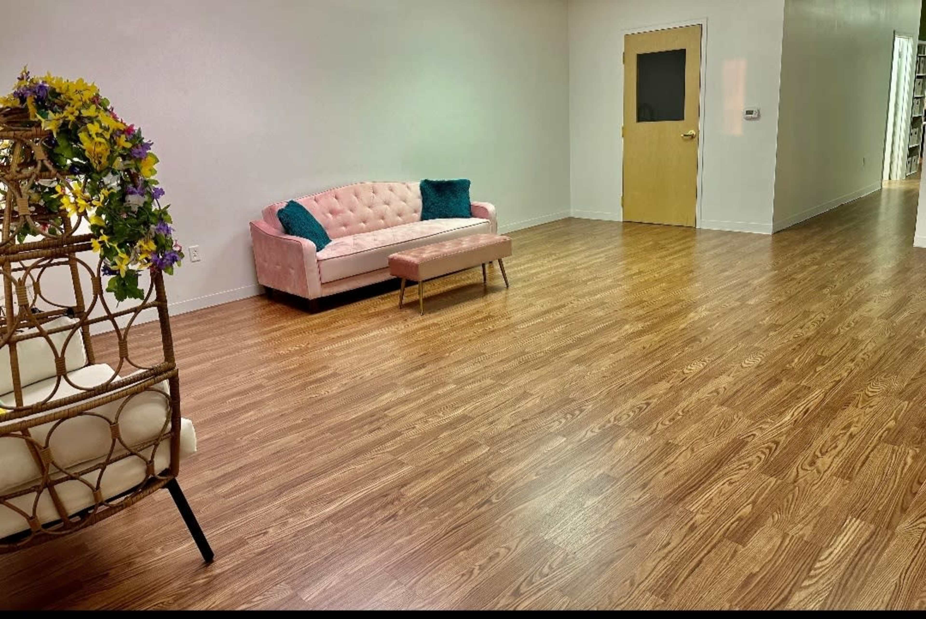 The room features a pink sofa and a wooden coffee table on a polished floor with a door leading to another area.