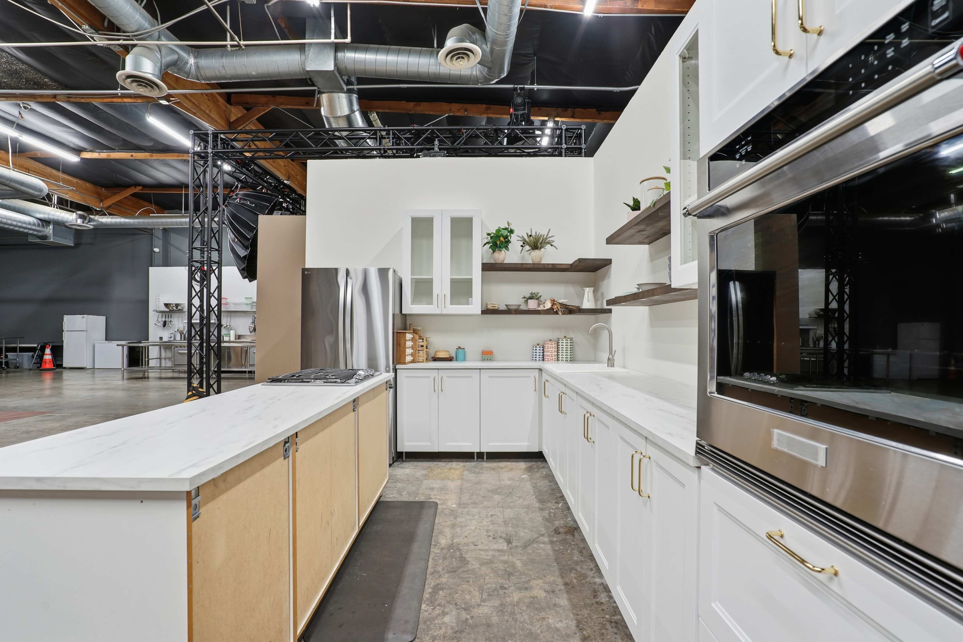 The image shows a modern kitchen setup featuring white cabinetry, a marble countertop, stainless steel appliances, and open shelving.