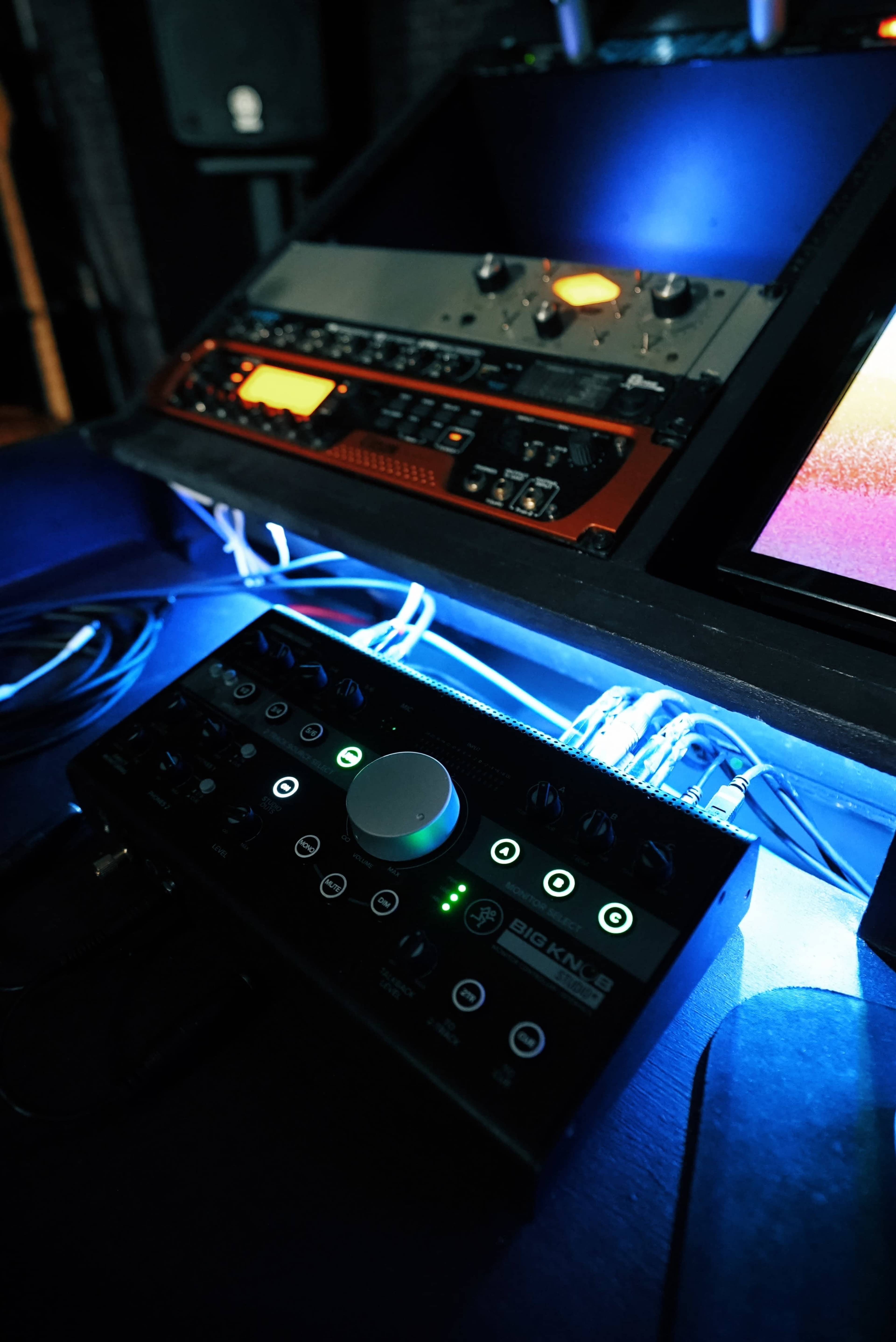 The image shows a close-up of an audio mixing console and equipment, illuminated by blue lights, with a focus on a central control knob.