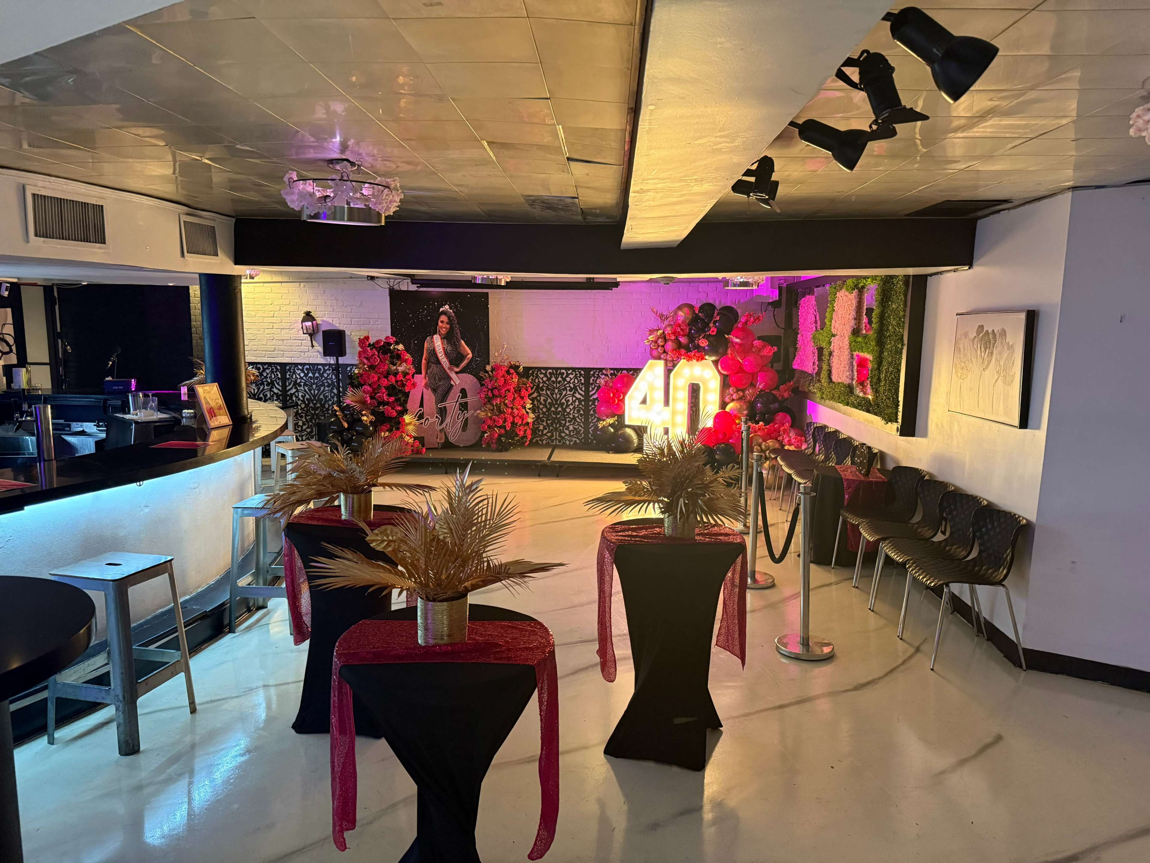 The image shows an elegantly decorated event space featuring tables with floral arrangements, a large "40" display, and vibrant lighting.