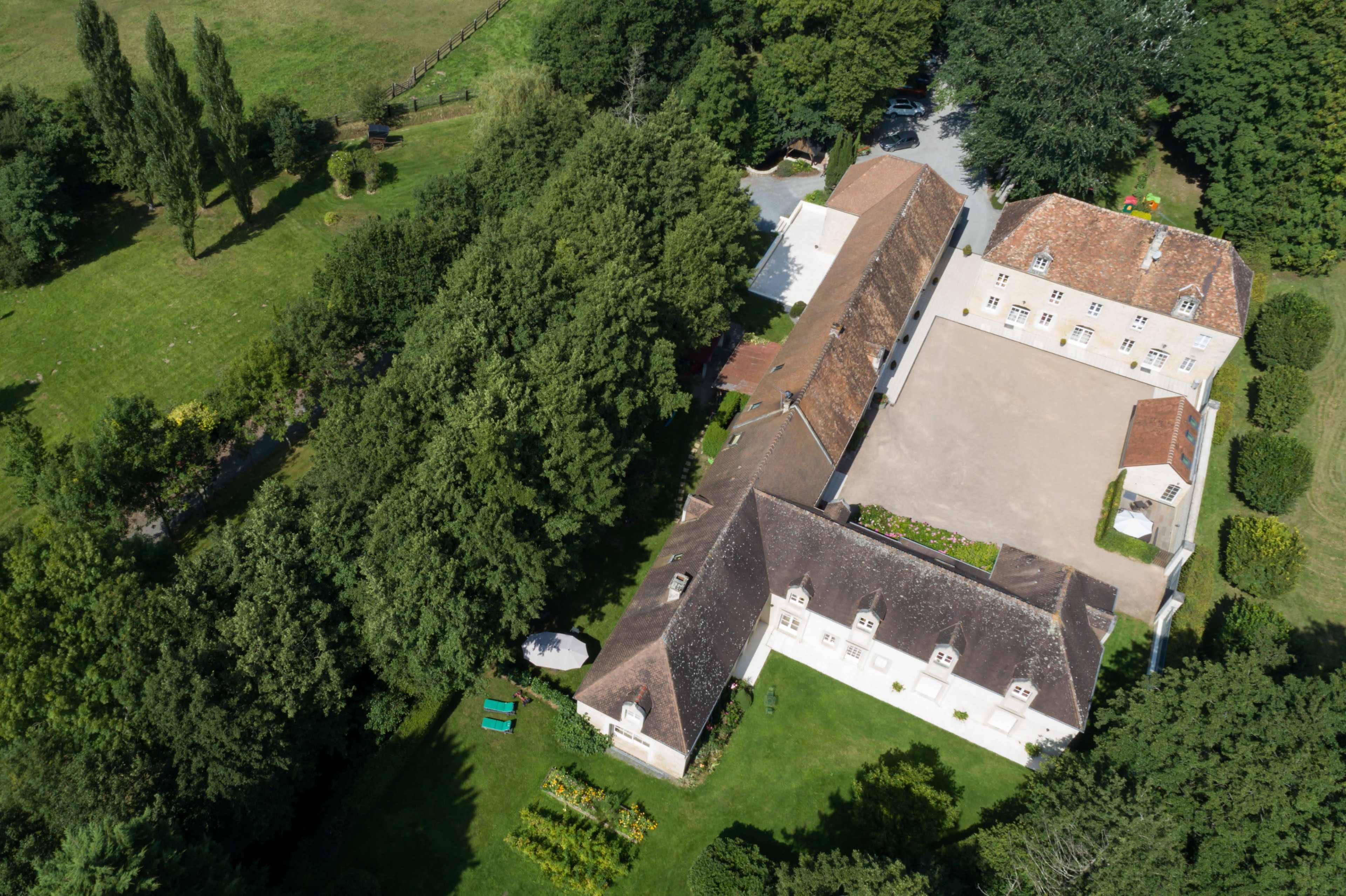 An aerial view shows a large estate surrounded by trees, featuring multiple buildings and a courtyard.