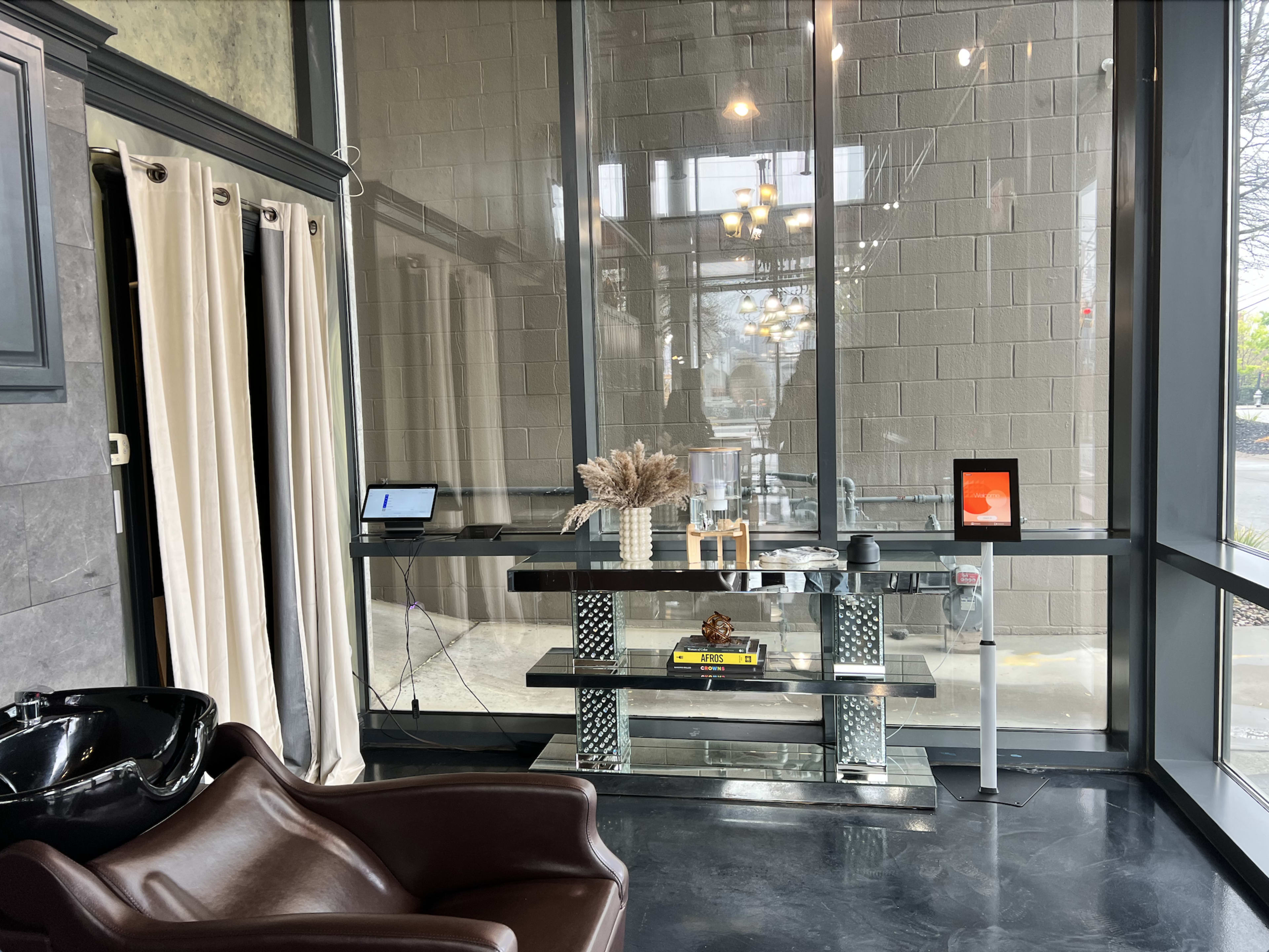The image shows a modern interior space with a glass wall, featuring a sleek table with decorative items and a cozy brown chair.