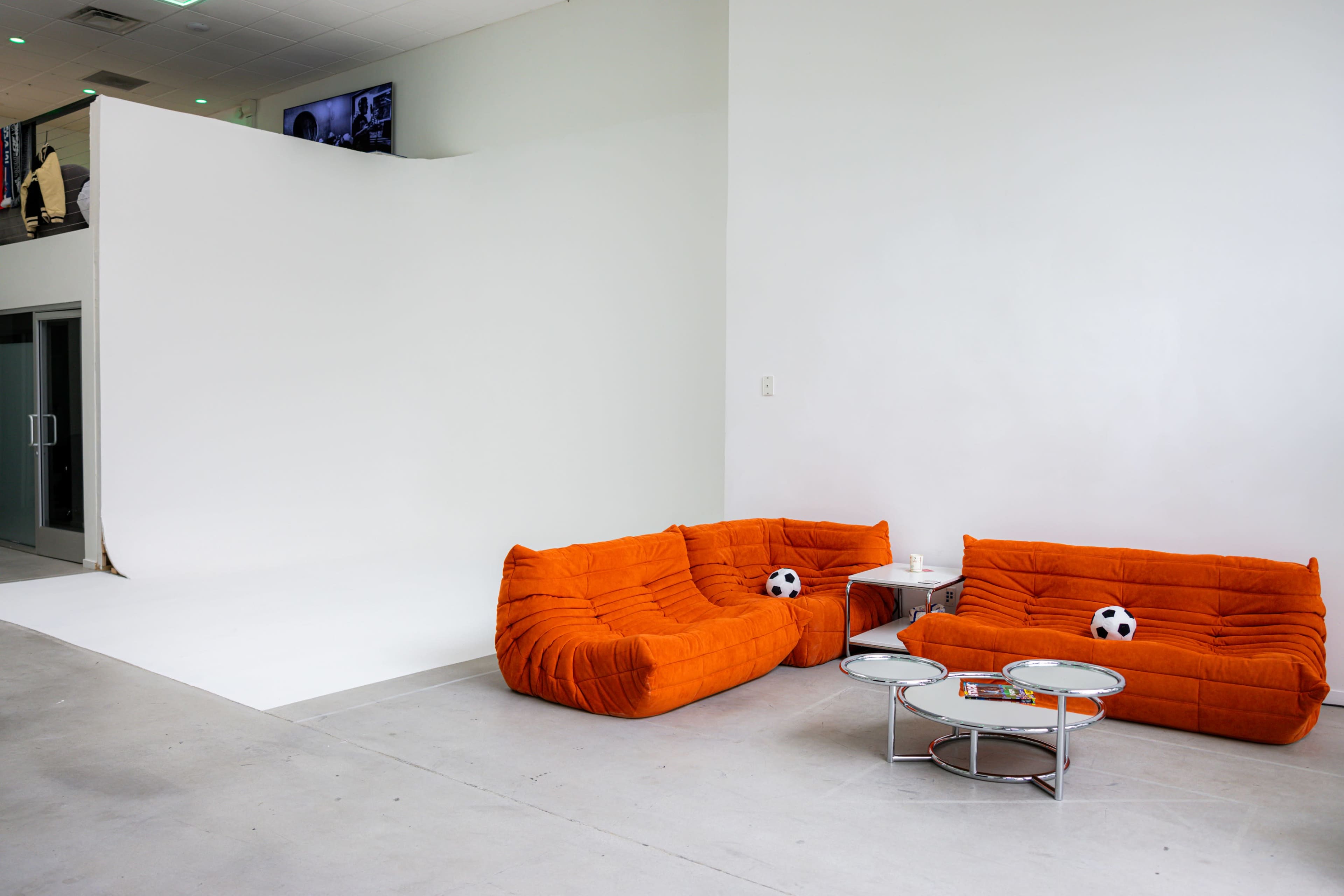 A minimalist interior featuring two orange, plush couches with soccer balls placed on them, accompanied by a round glass coffee table.