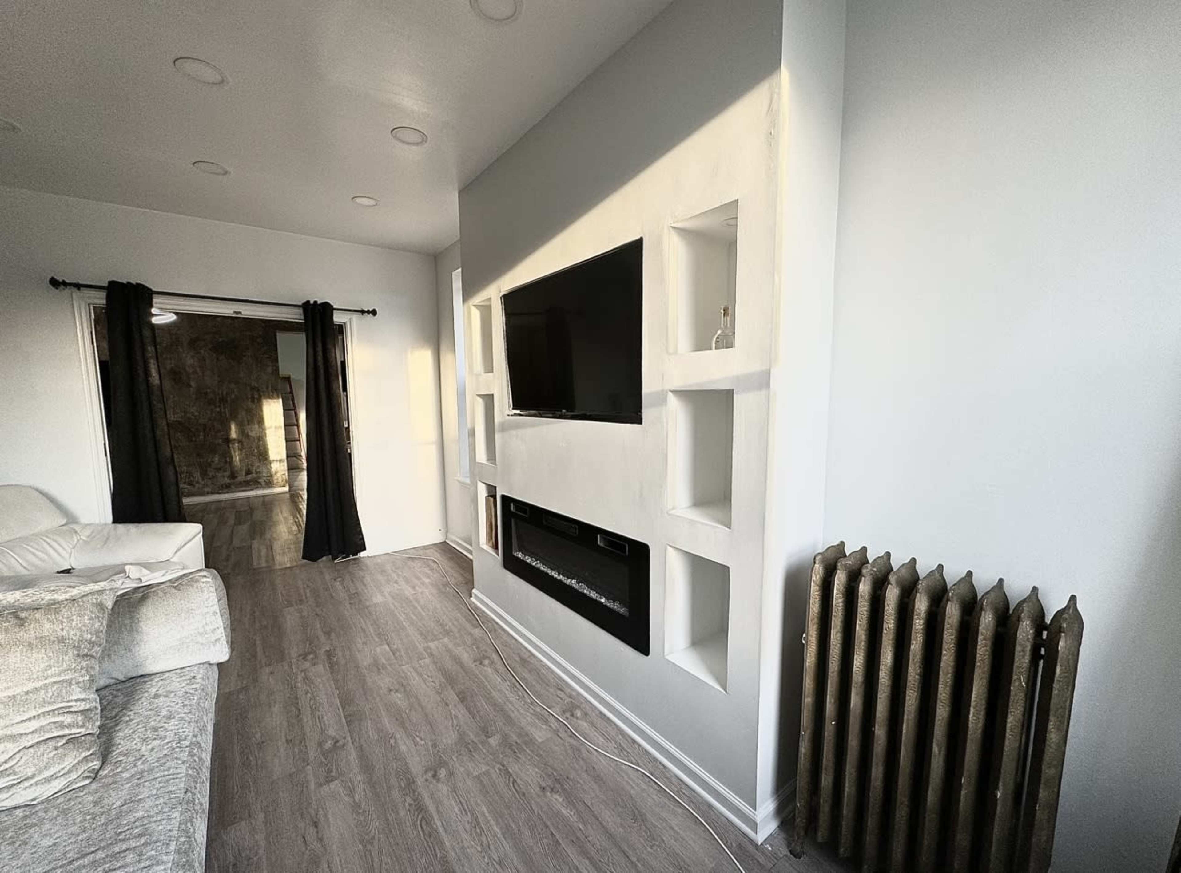 A modern living room with a wall-mounted television, built-in shelves, an electric fireplace, and a vintage-style radiator.