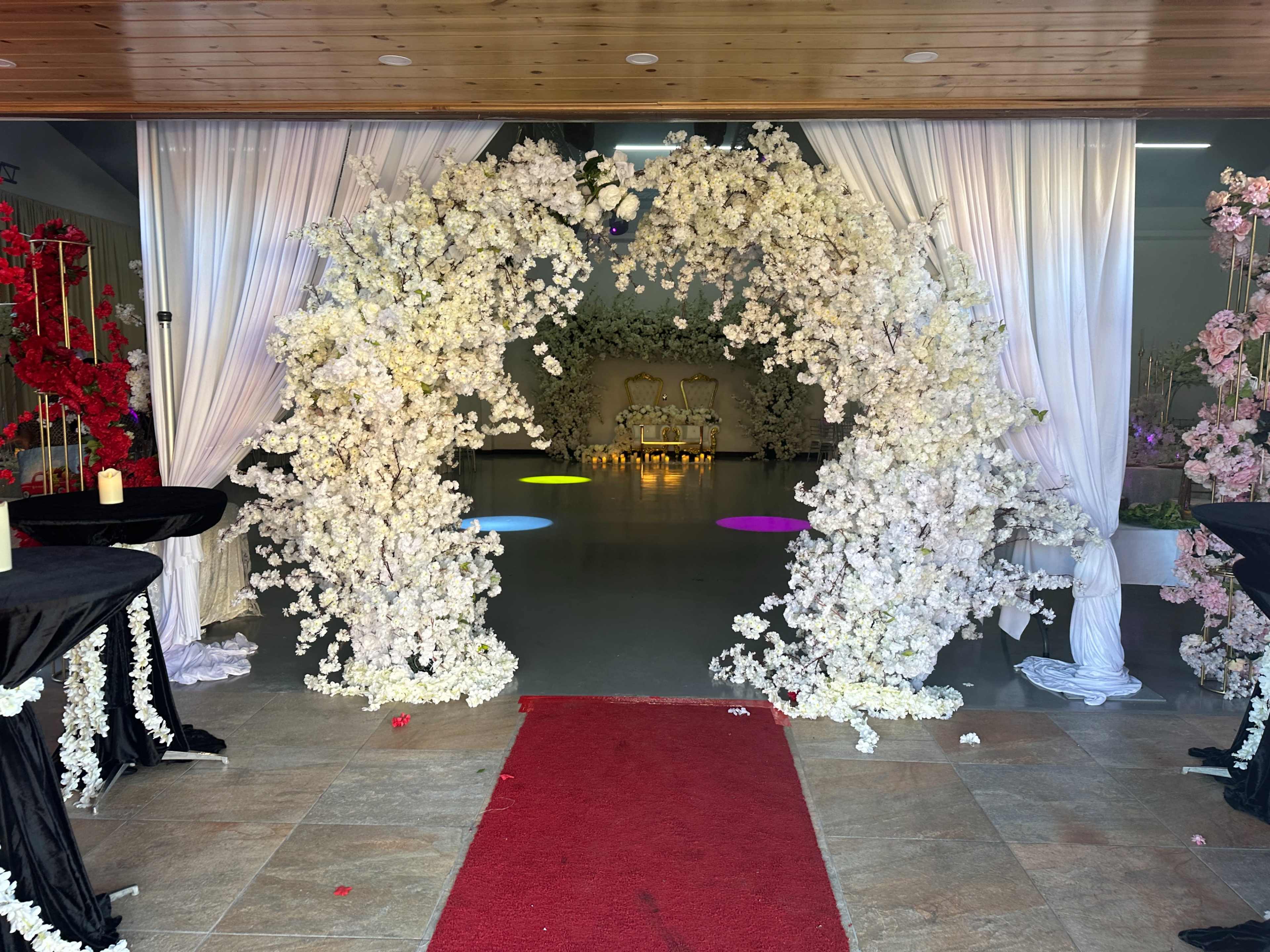 A floral arch adorned with white flowers leading into a decorated indoor space with illuminated areas on the floor.