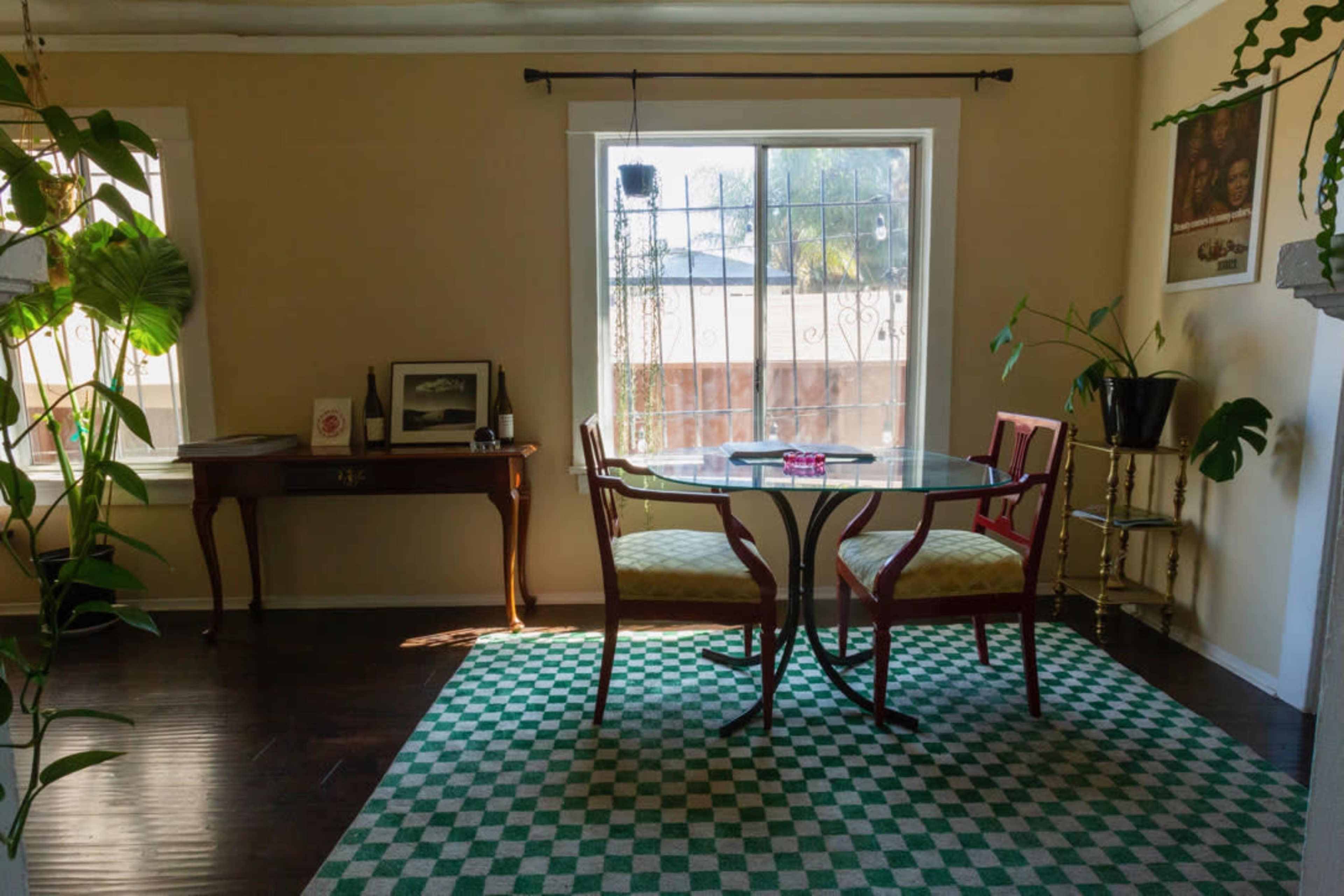 A small dining area features a round table set for two, with a patterned rug on the floor and a window that allows natural light to enter.