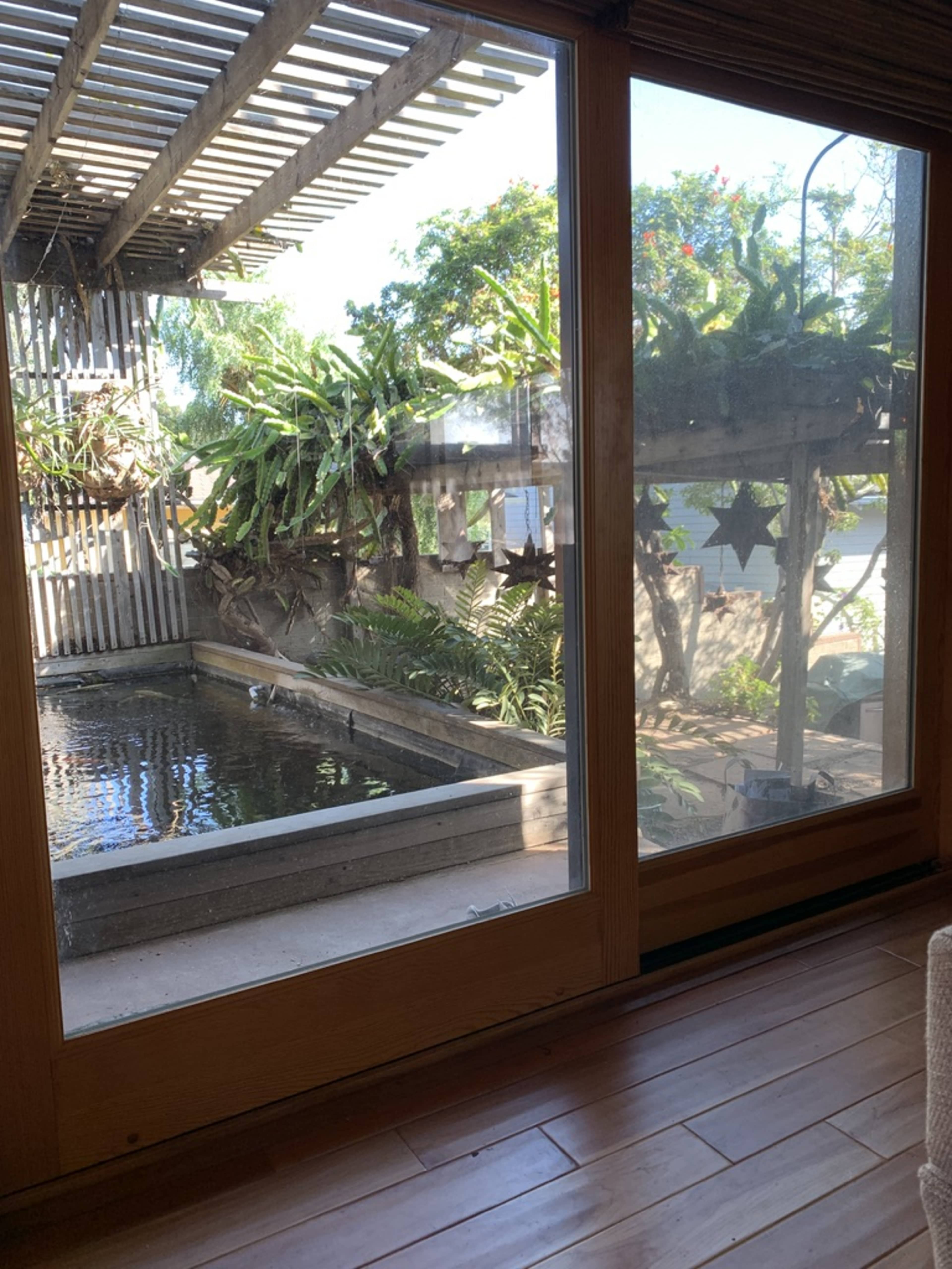 A large glass window overlooking a serene outdoor space with a pond, greenery, and wooden structures.