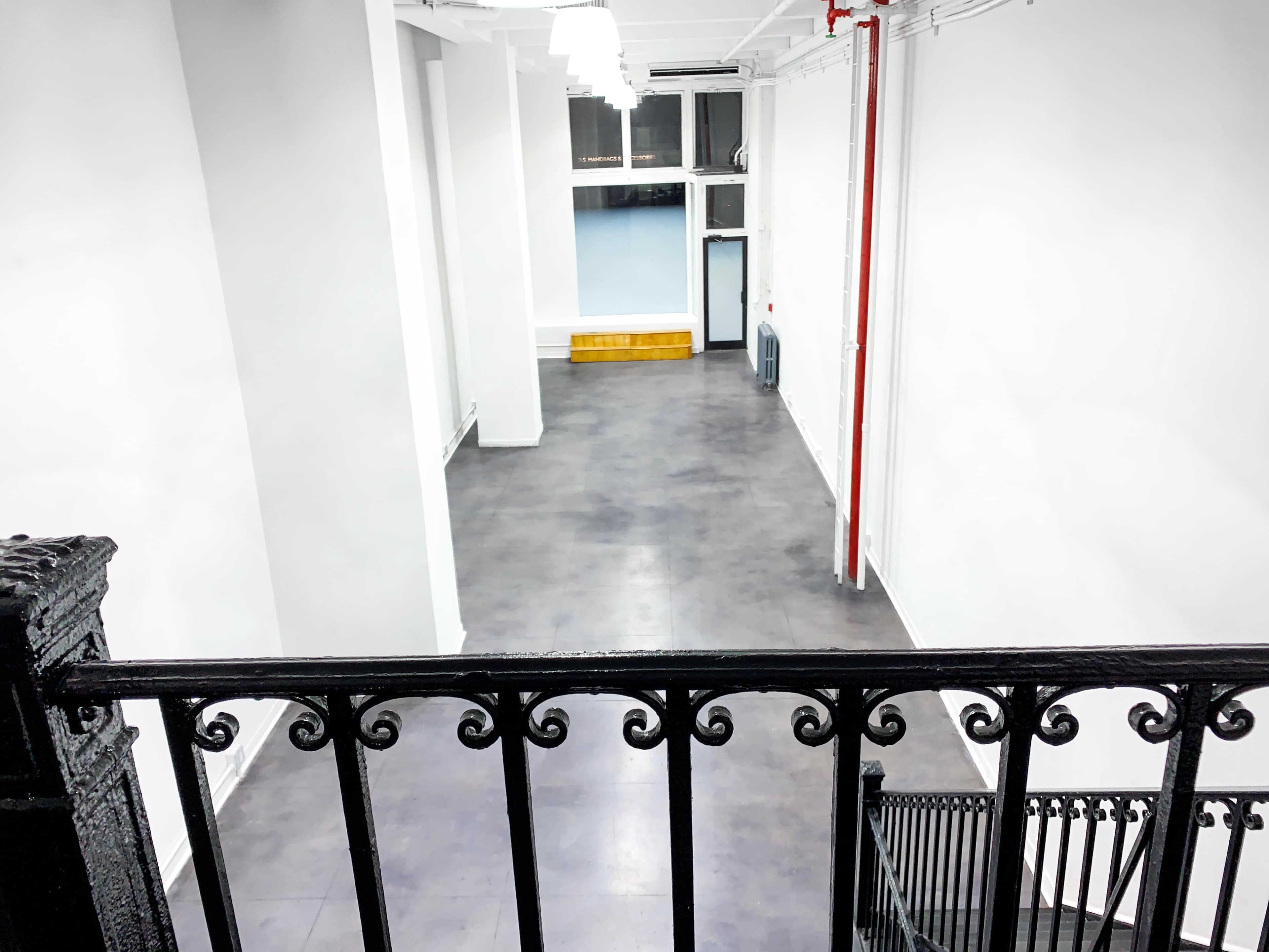 A spacious, empty room with gray flooring and white walls, viewed from a balcony railing.