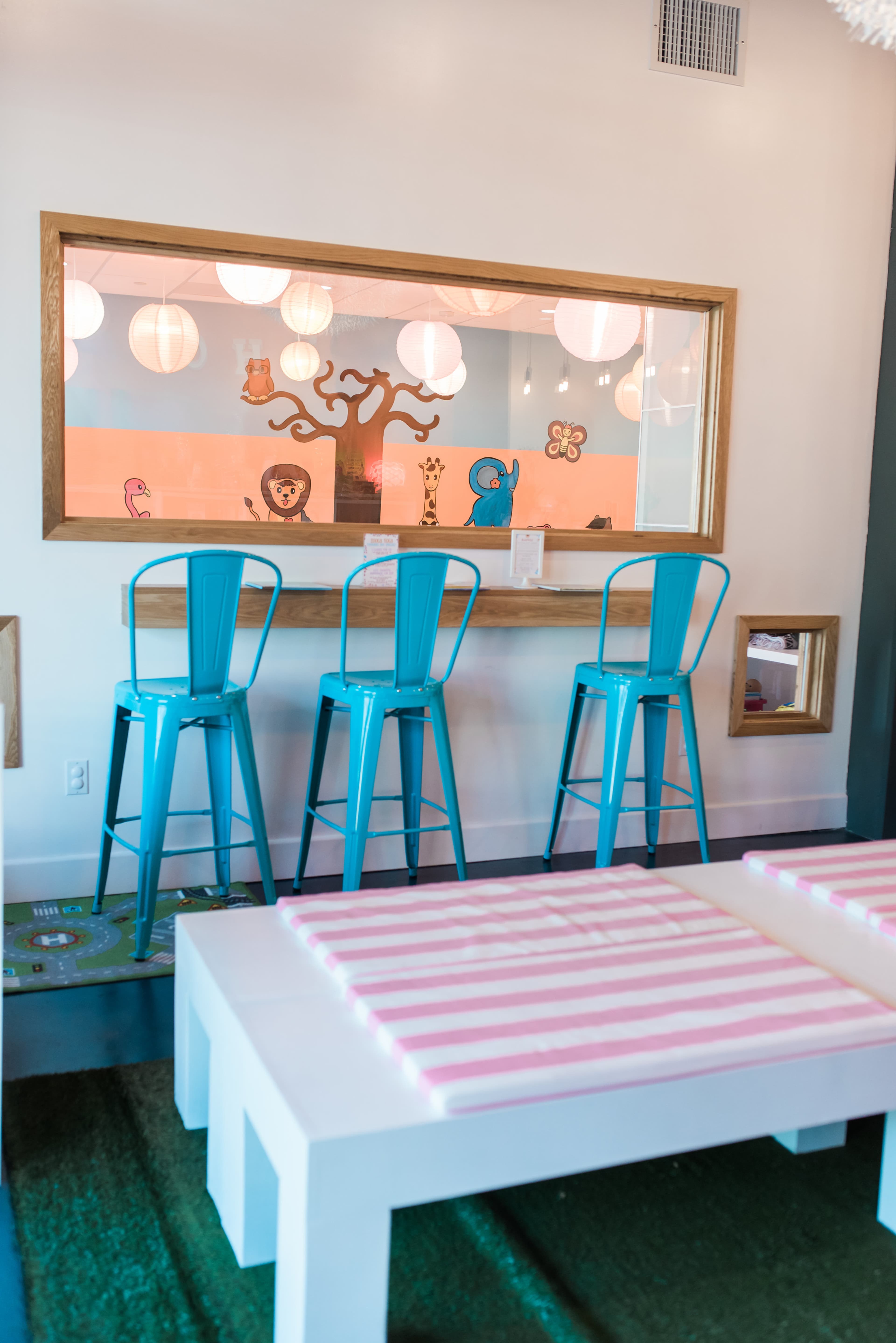 A brightly lit room featuring a seating area with turquoise bar stools and a large window overlooking a colorful play area.