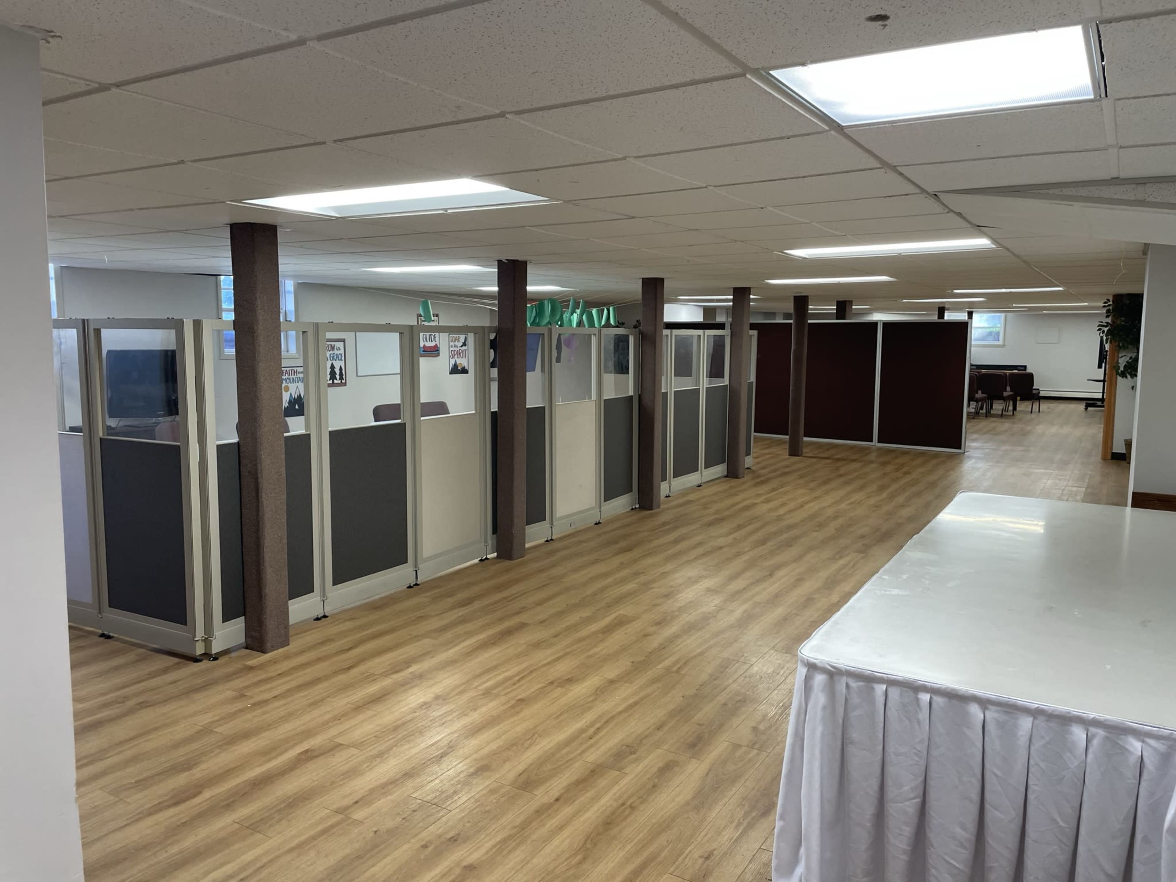 A spacious office area with cubicles lined along one side and a blank table in the foreground.