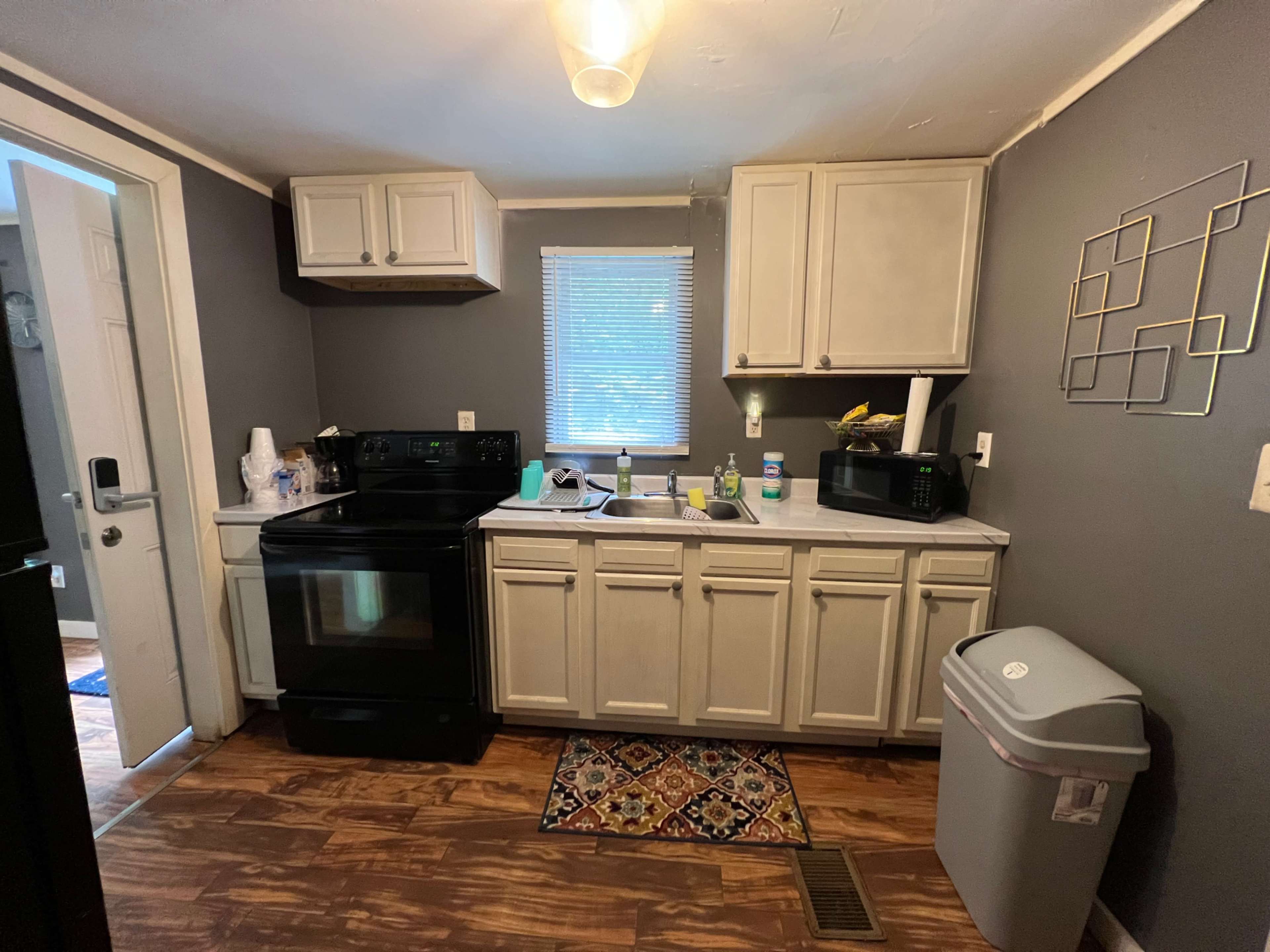 A small kitchen with white cabinets, a black stove, and a sink area with various kitchen items and appliances.