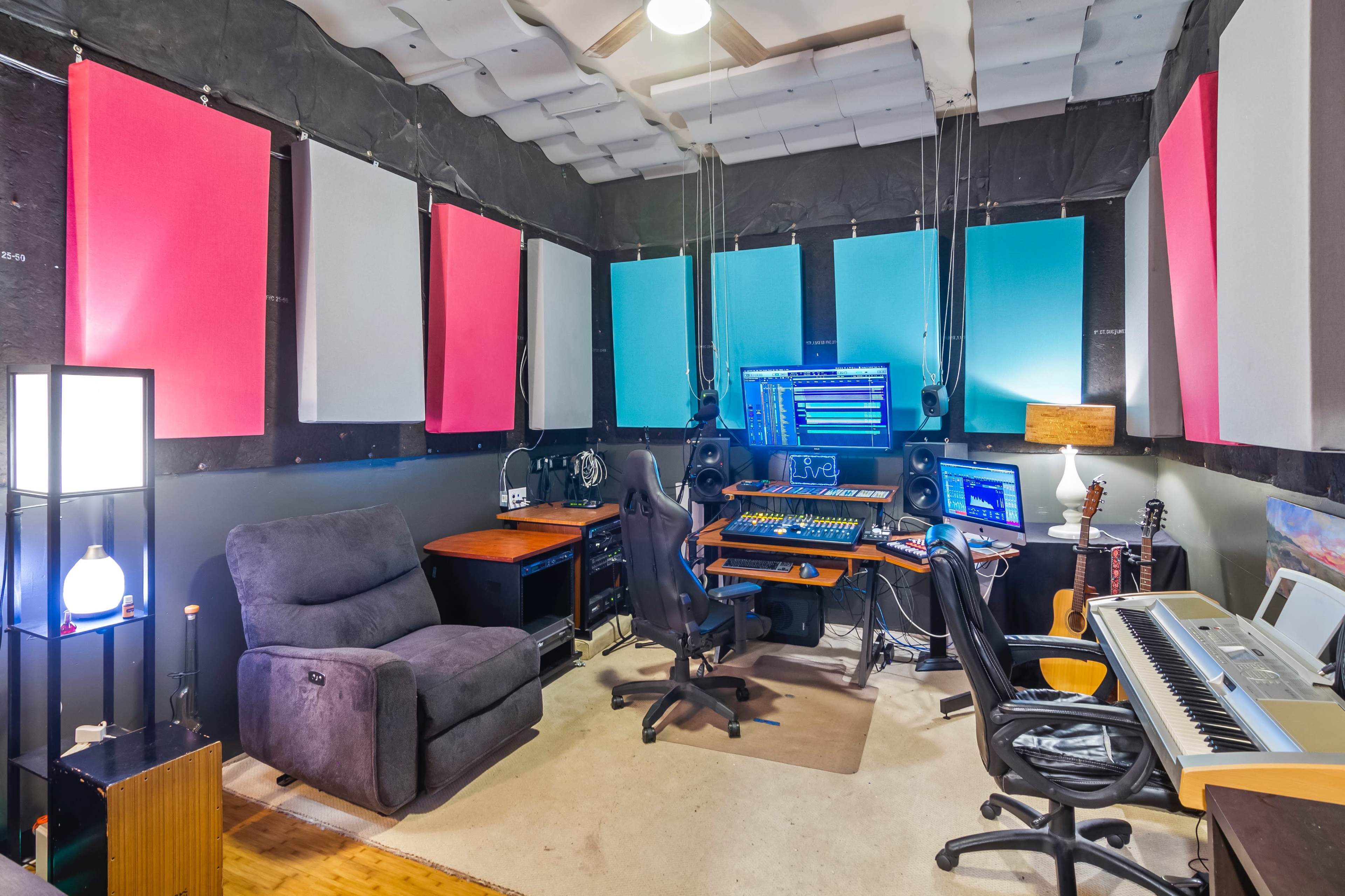 A music production studio features soundproofed walls, a computer workstation with monitors, and multiple seating areas.