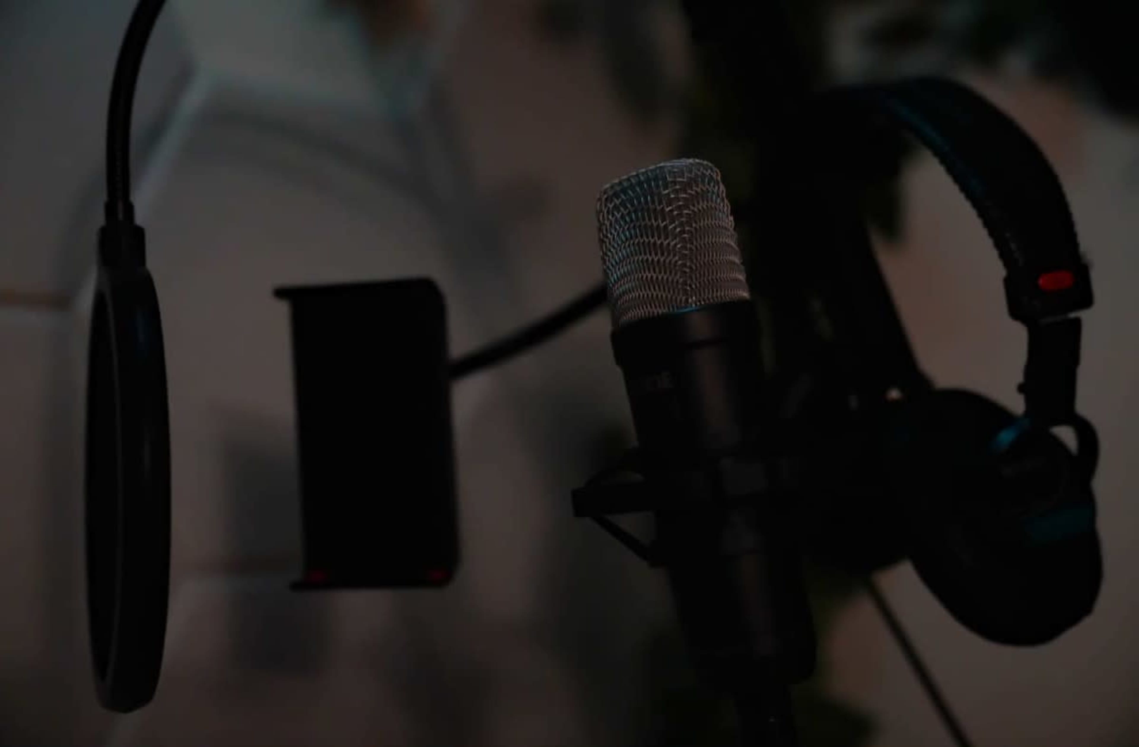 A microphone and headphones are prominently positioned in a dimly lit recording studio setup.