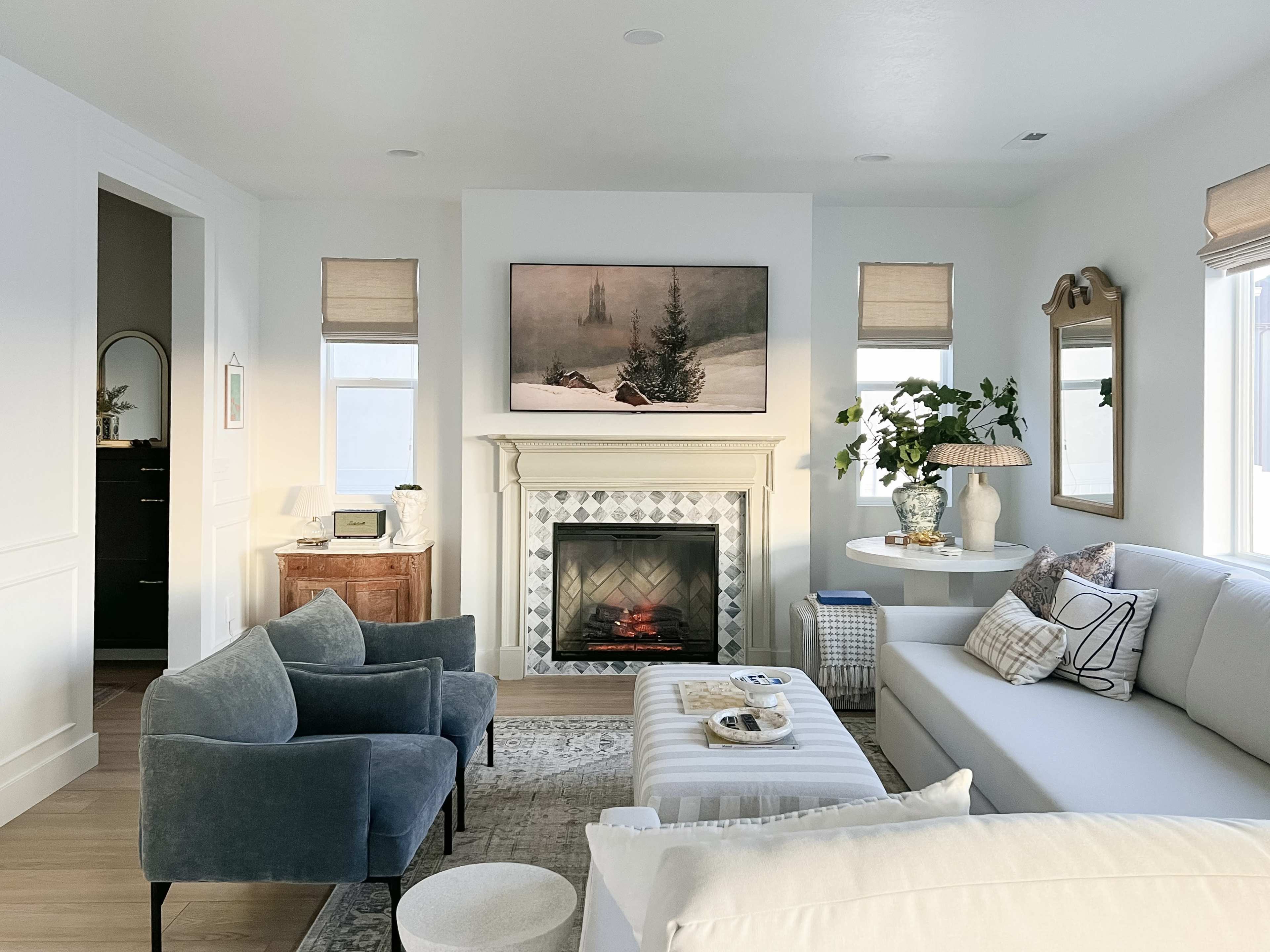 A modern living room featuring a fireplace, a large wall-mounted television displaying a winter scene, and a combination of light-colored furniture and decor.