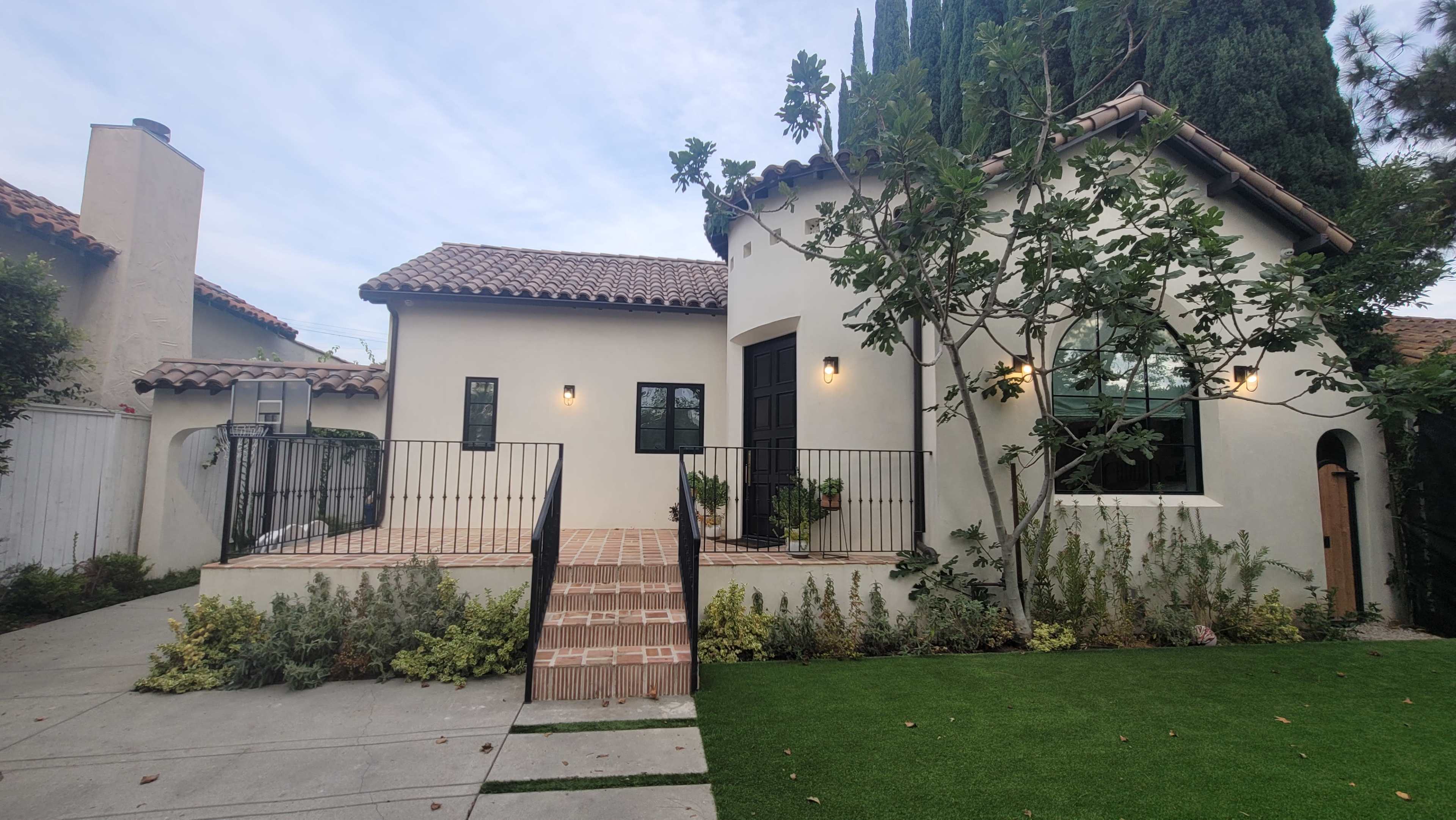 A modern house with a tiled roof, a front patio, and a landscaped yard featuring shrubs and greenery.