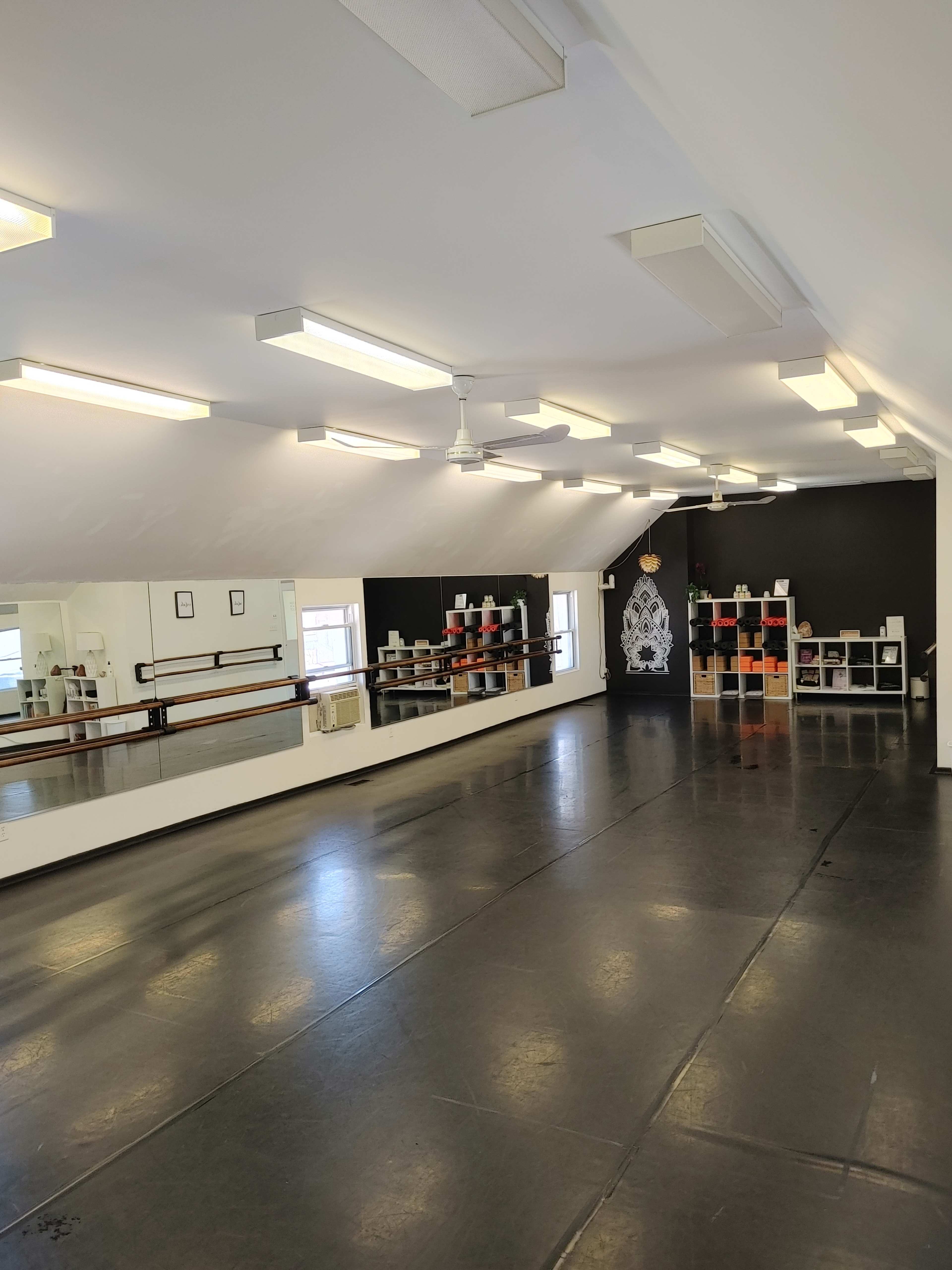 An empty dance studio with mirrored walls, black flooring, and shelves of colorful blocks along one side.