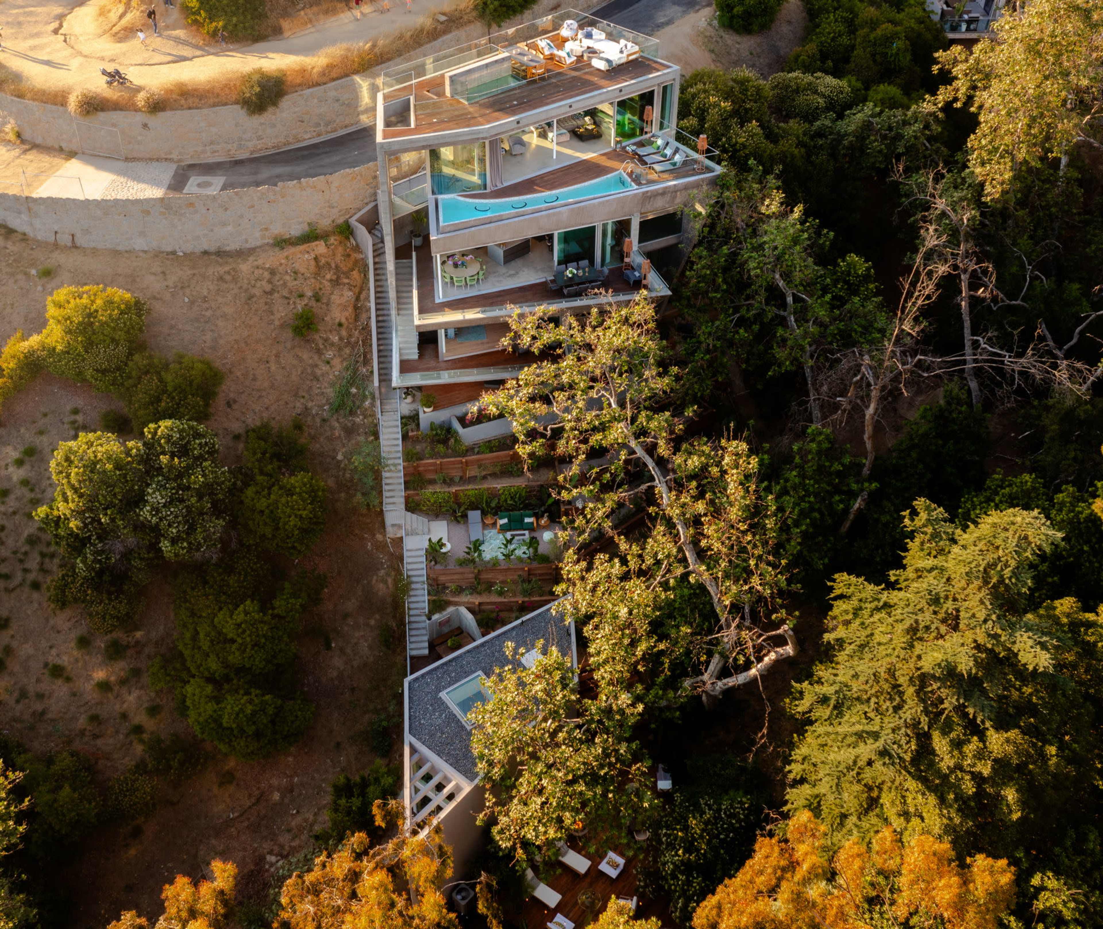A modern multi-level house built into a hillside, surrounded by trees and greenery.
