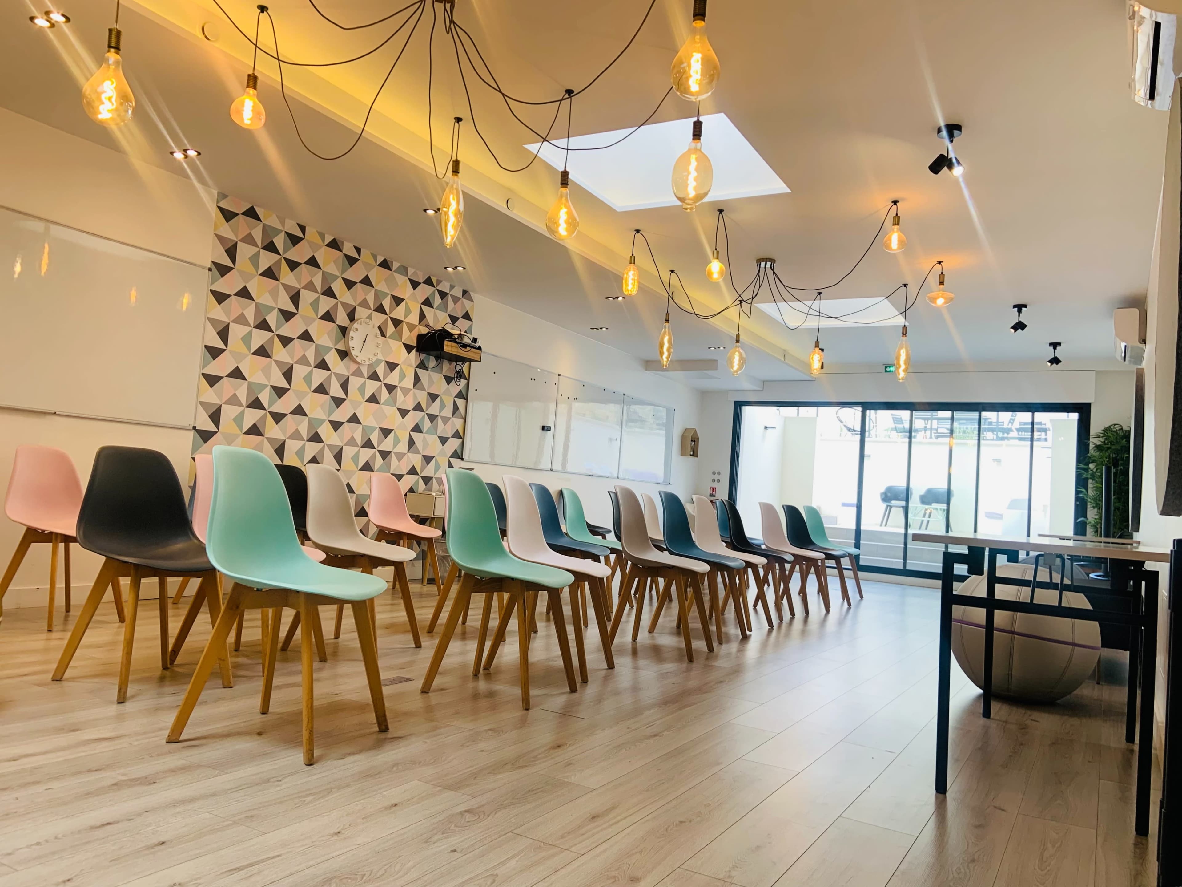 A modern meeting room with rows of colorful chairs arranged in front of a patterned wall and large windows that allow natural light to enter.