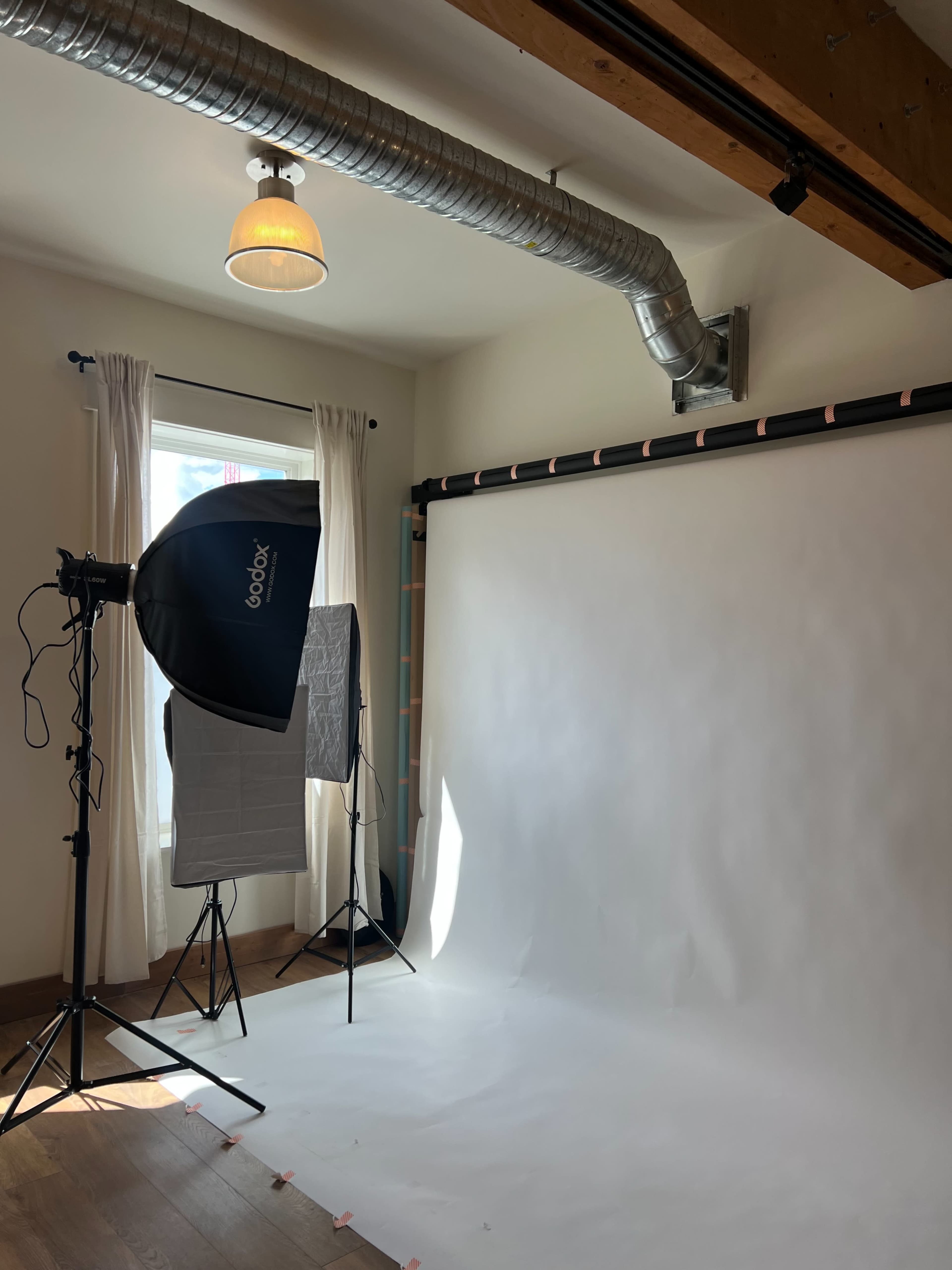 An empty photography studio features a backdrop, lighting equipment, and natural light from a window.