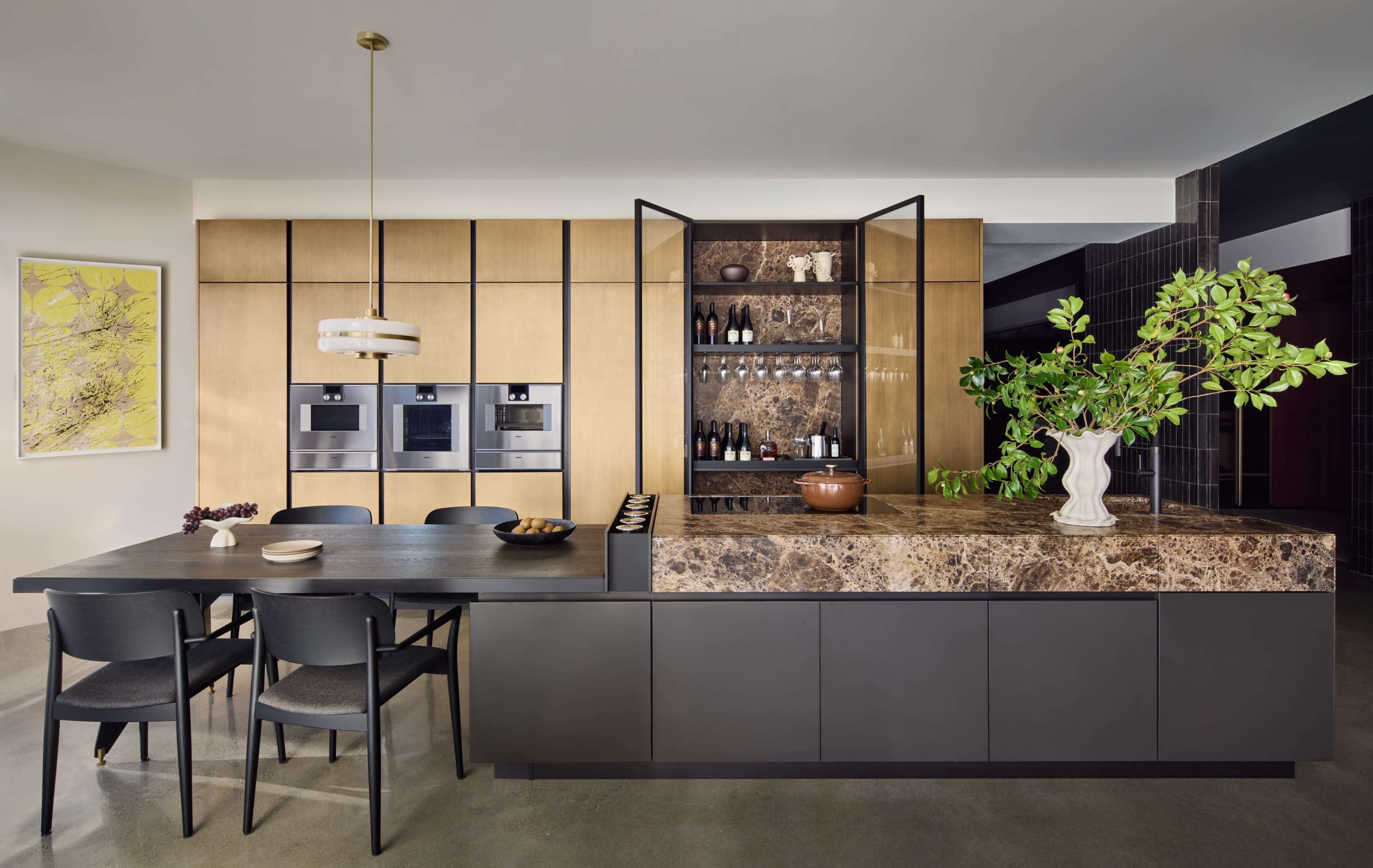 The image shows a modern kitchen with a large island featuring a brown marble countertop, sleek cabinetry, and an open shelving unit displaying wine bottles.