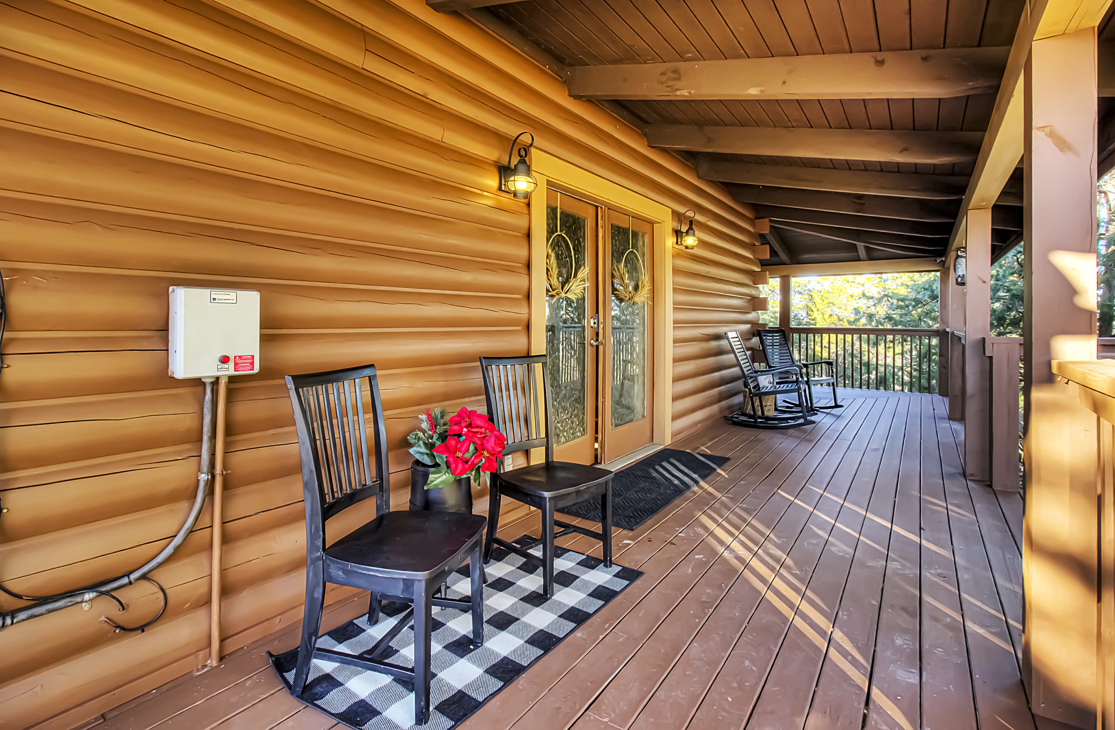 The image shows a wooden porch with two black chairs and a small red plant on a checkered mat near the entrance.