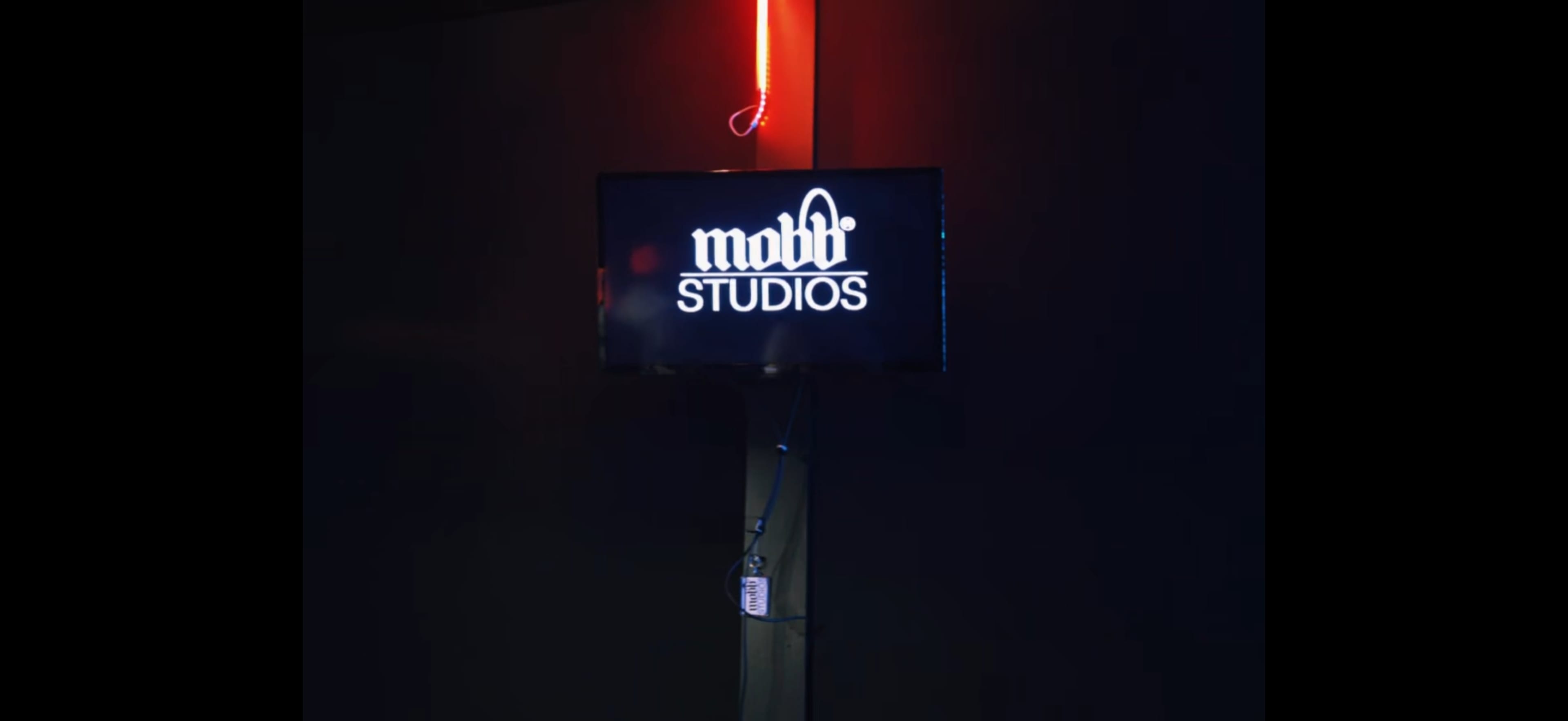 The image shows a television displaying the logo of "mobb Studios" against a dark backdrop, with a red neon light visible in the upper area.
