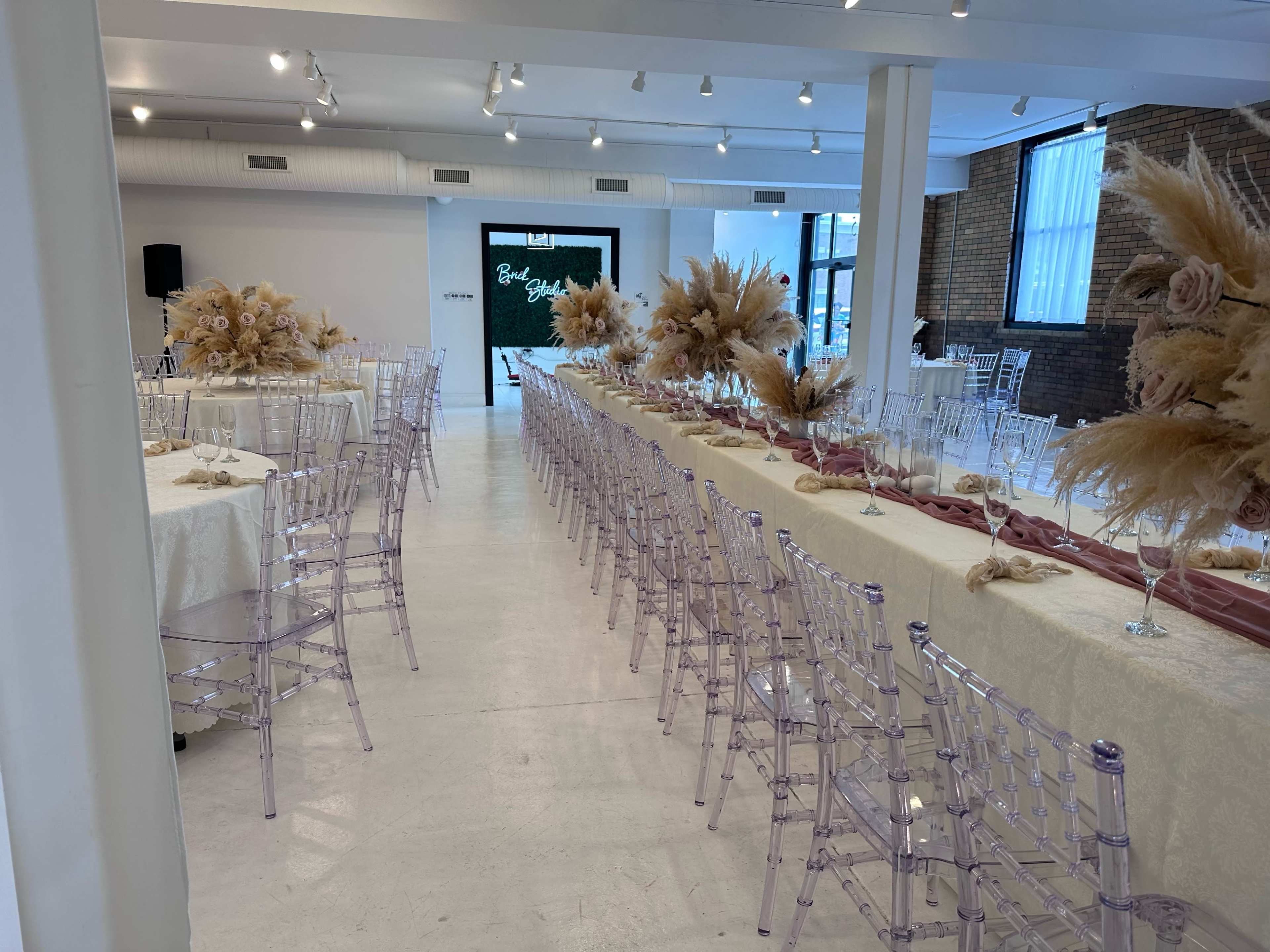A spacious event hall features long tables set with elegant decor and floral arrangements, illuminated by bright overhead lights.