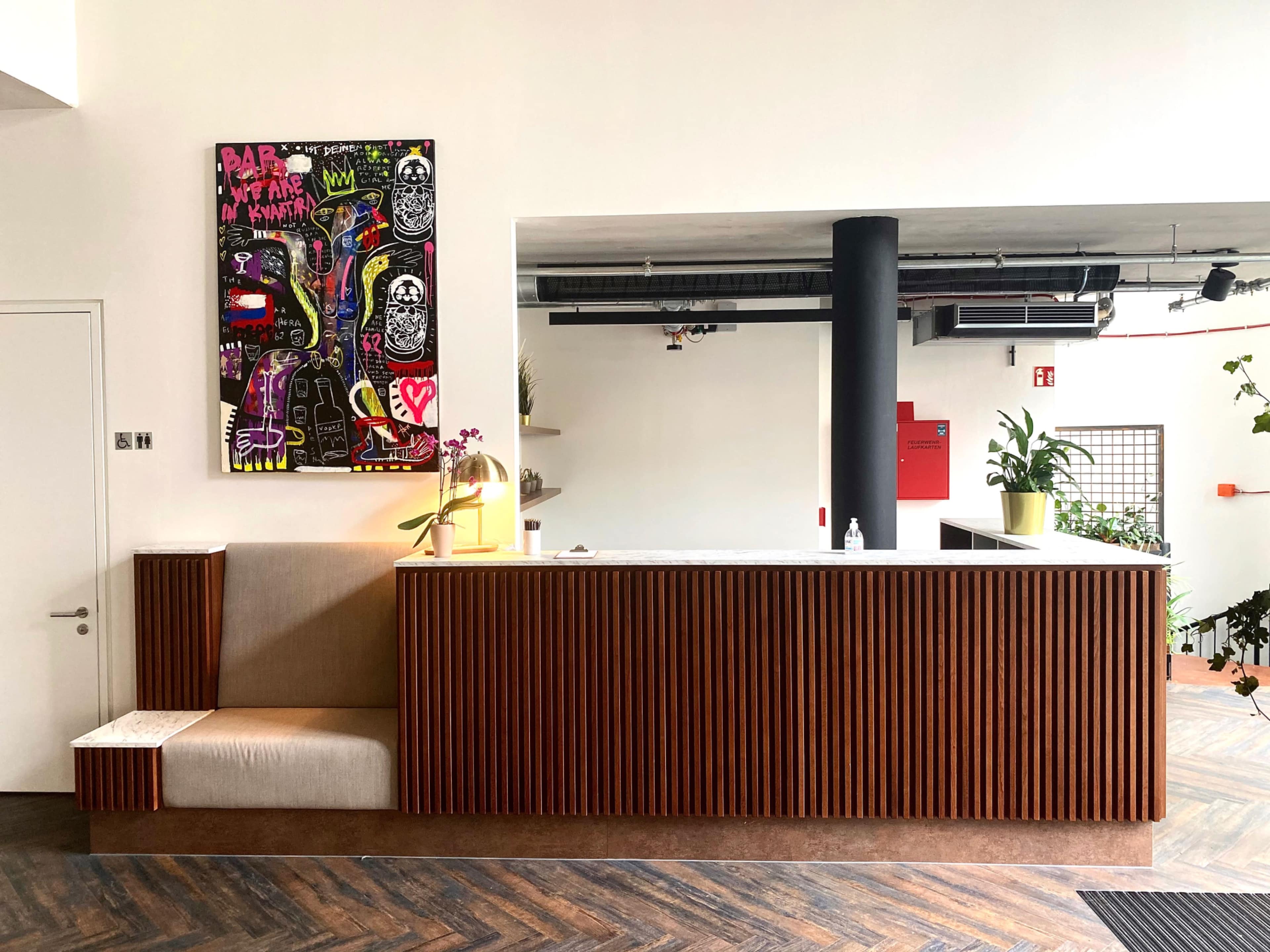 The image shows a modern reception area with a wooden counter and a large colorful artwork on the wall behind it.