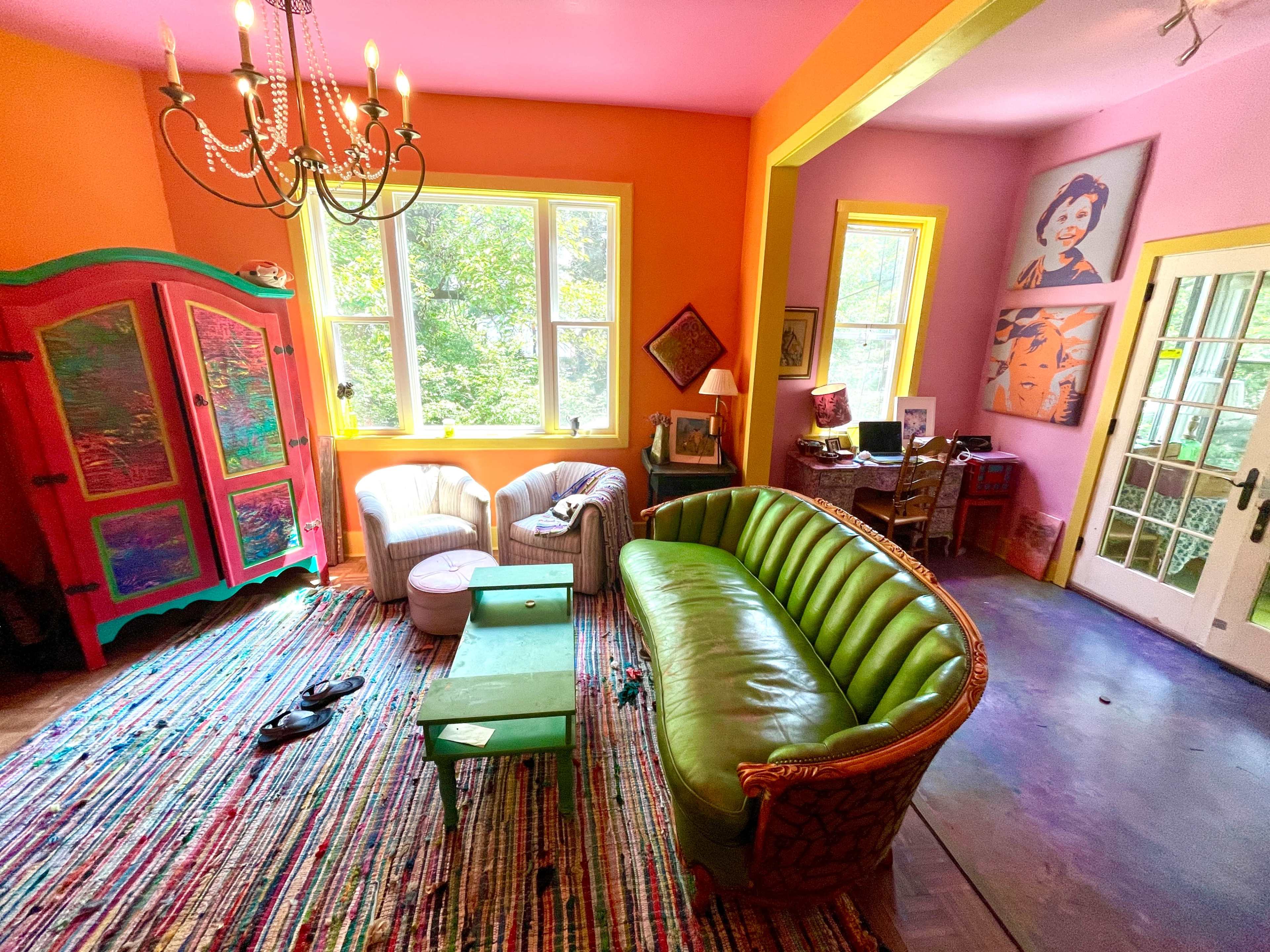 The image shows a brightly colored living room with a green sofa, colorful walls, a patterned rug, and an eclectic mix of furniture and decor.