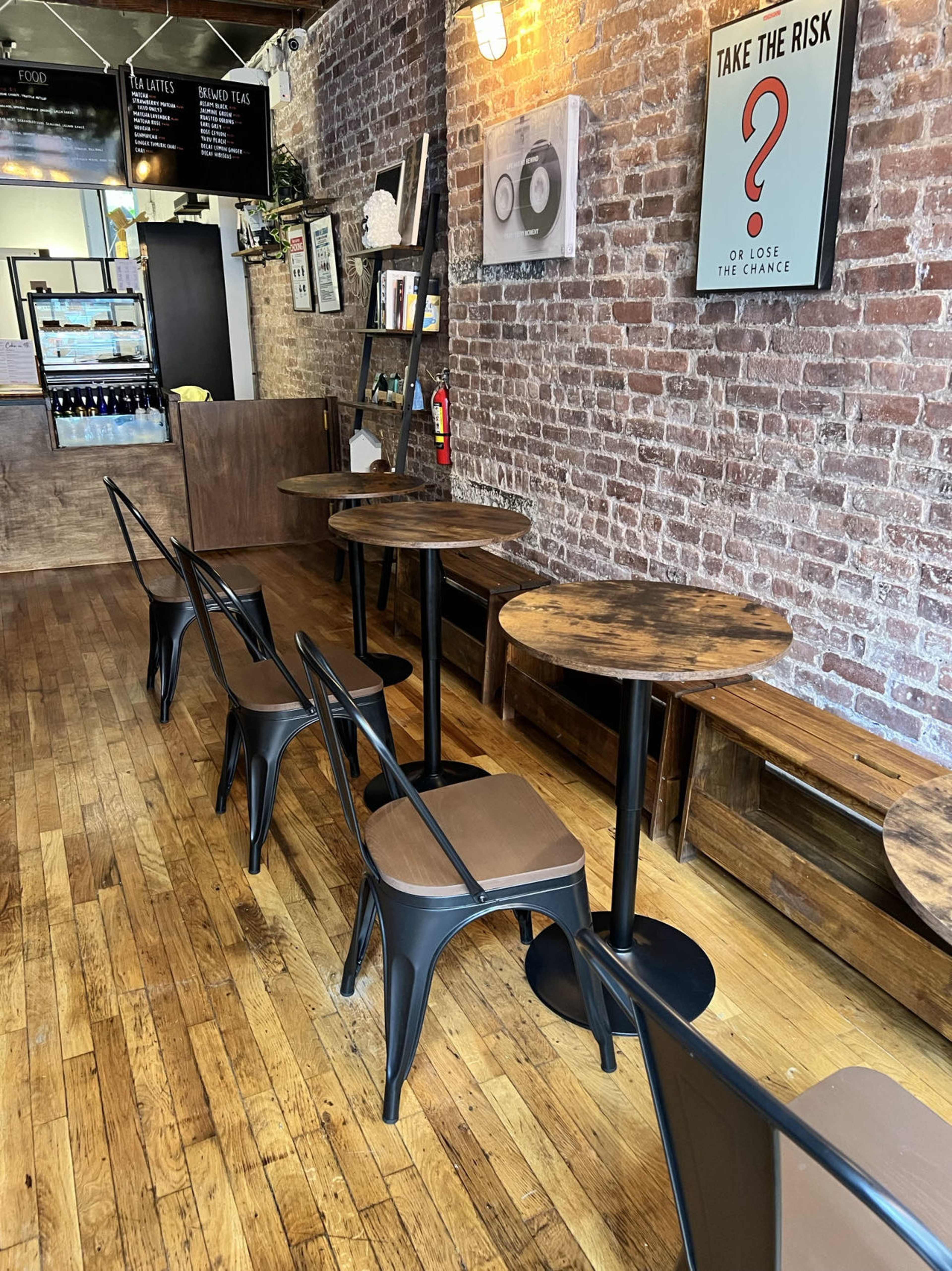 A cozy café with wooden floors, brick walls, and several round tables surrounded by metal chairs.