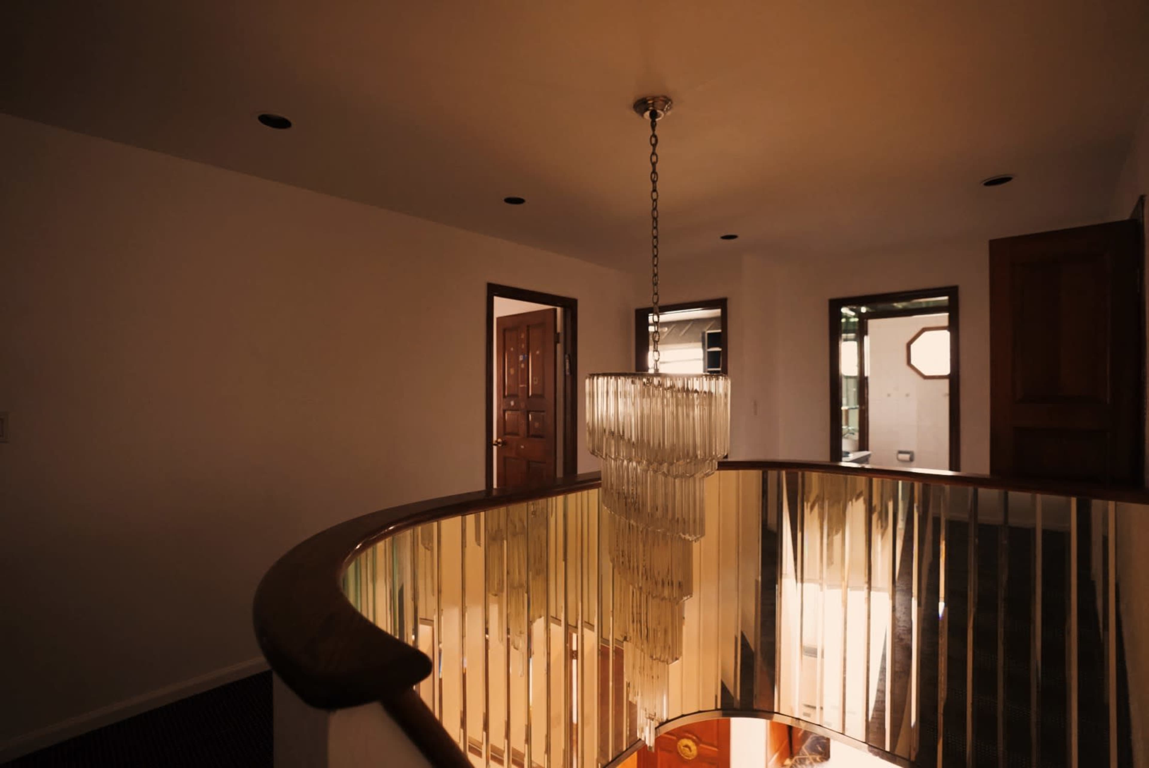 A spiral staircase leads to an upper hallway with a modern chandelier illuminating the space.
