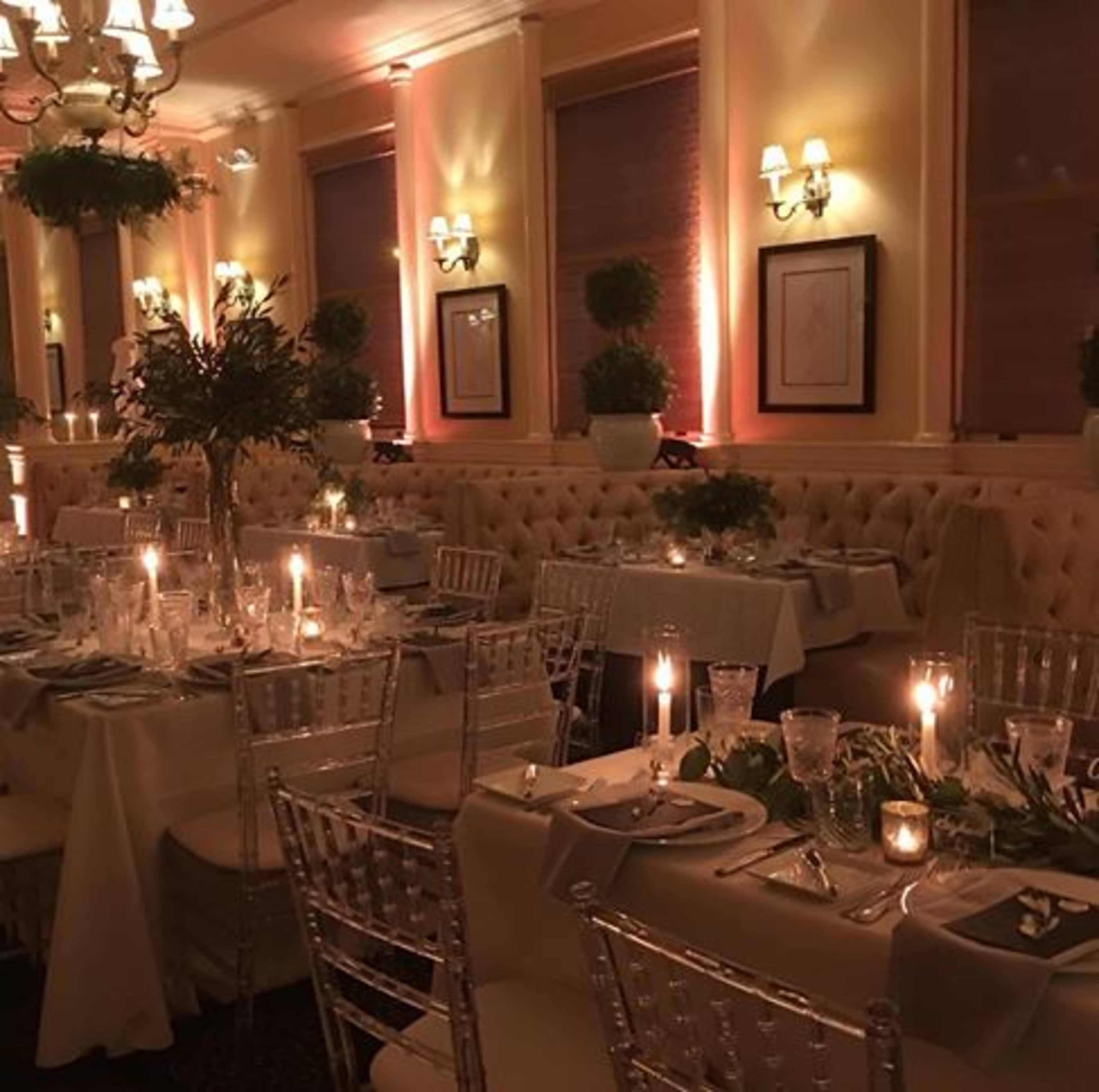A dining area with elegantly set tables, lit by candles, in a restaurant featuring soft lighting and decorative greenery.