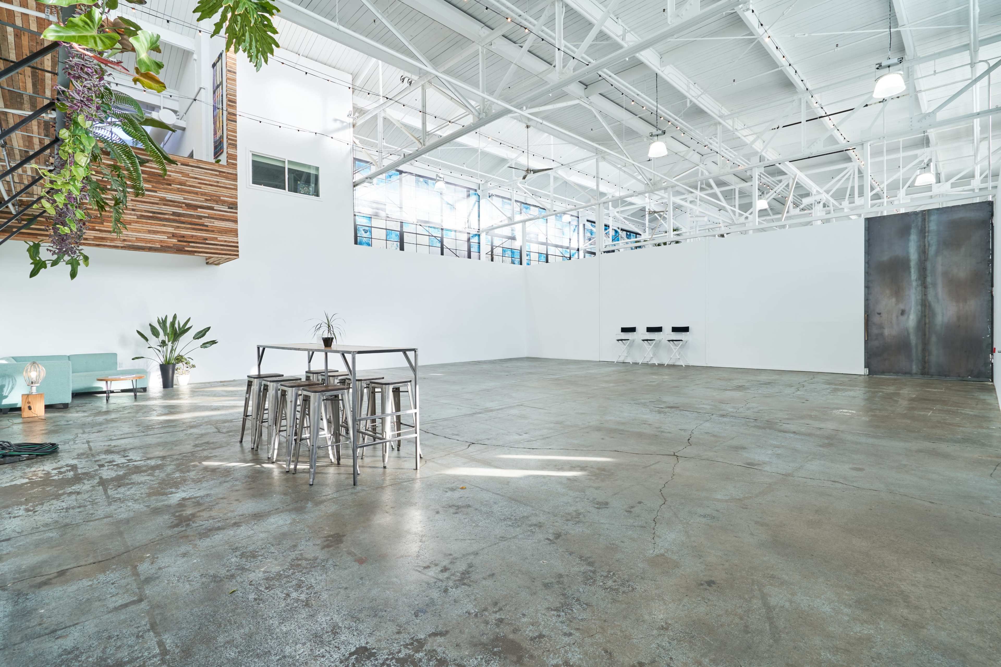 A spacious, minimally furnished industrial room with concrete flooring and large windows.