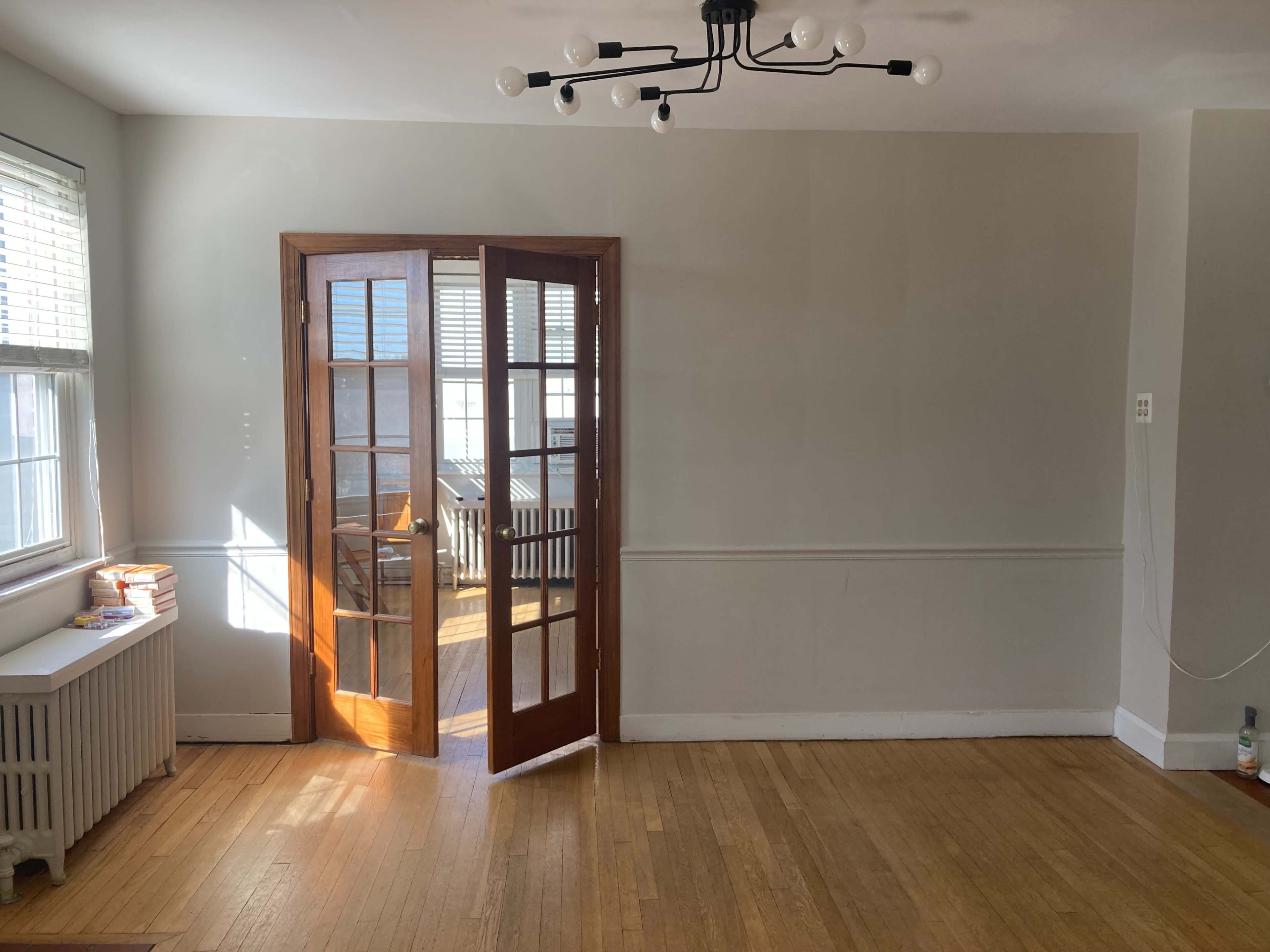 A set of French doors opens into a well-lit, empty room with wooden floors and a radiator beneath a window.
