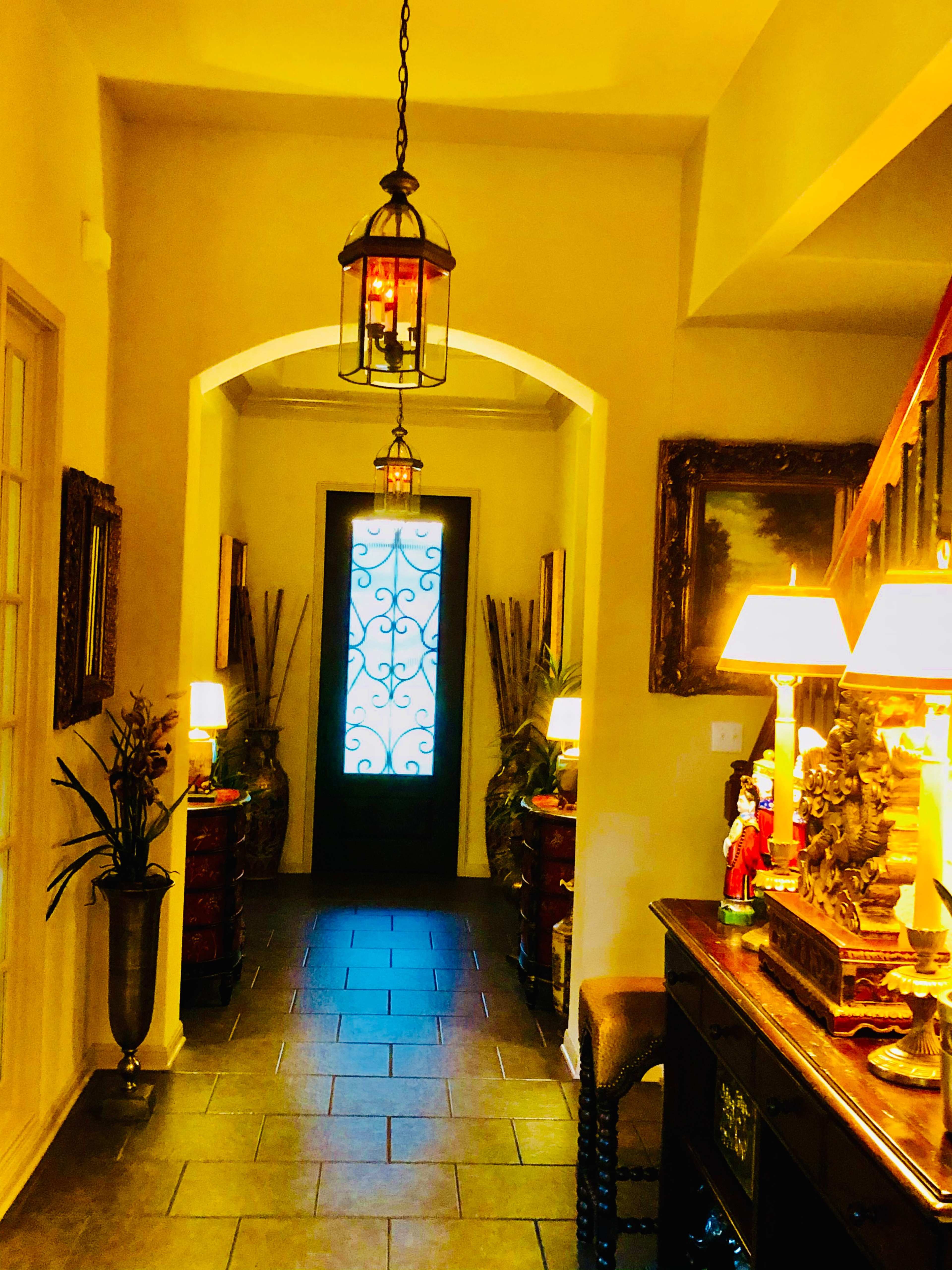 A well-lit hallway featuring a decorative entrance door, lanterns hanging from the ceiling, and various pieces of furniture along the walls.