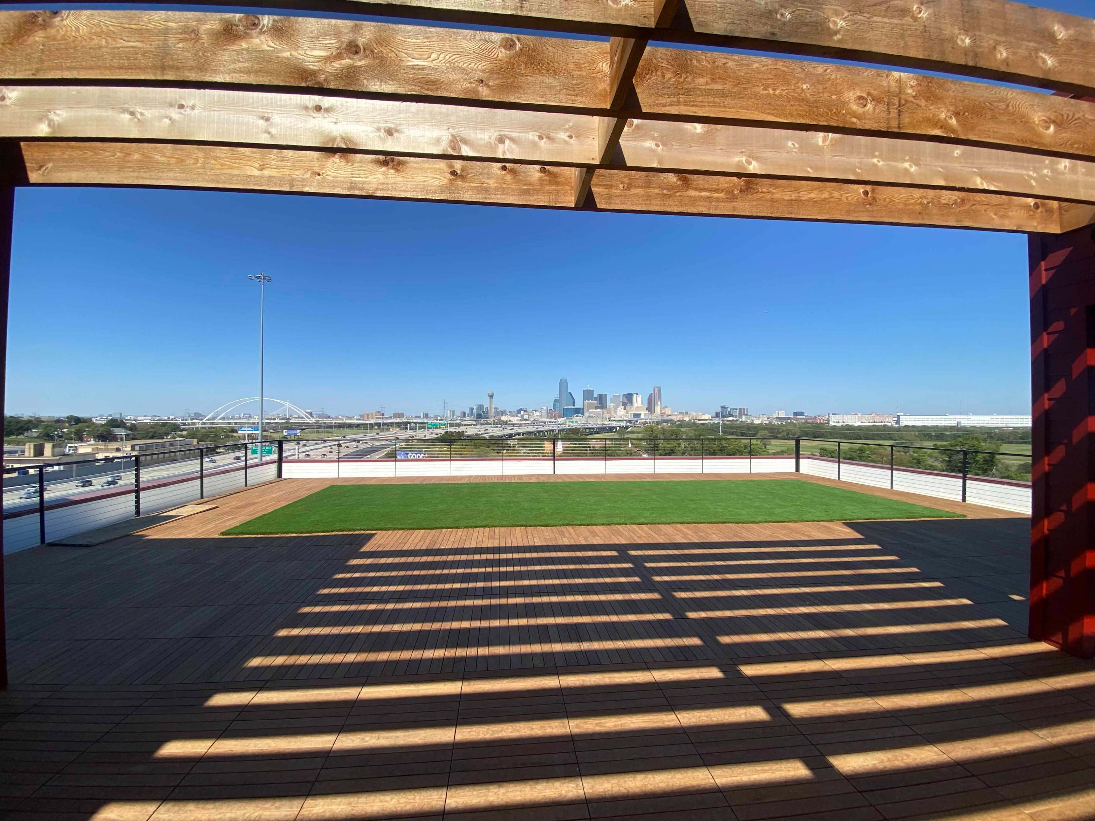 A rooftop terrace features wooden beams and a view of a city skyline with a clear blue sky.