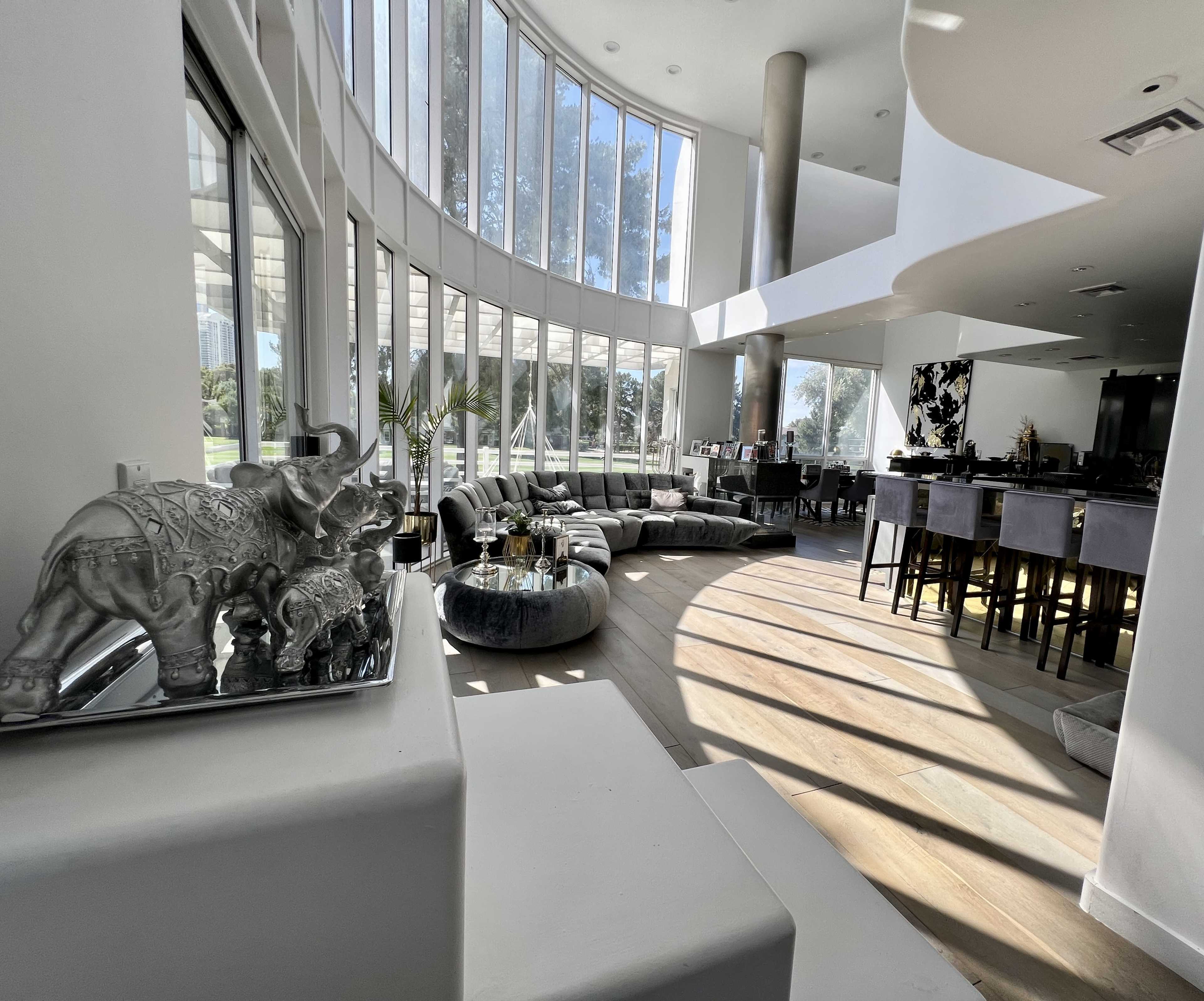 A spacious living area with large windows, modern furniture, and a view of greenery outside.