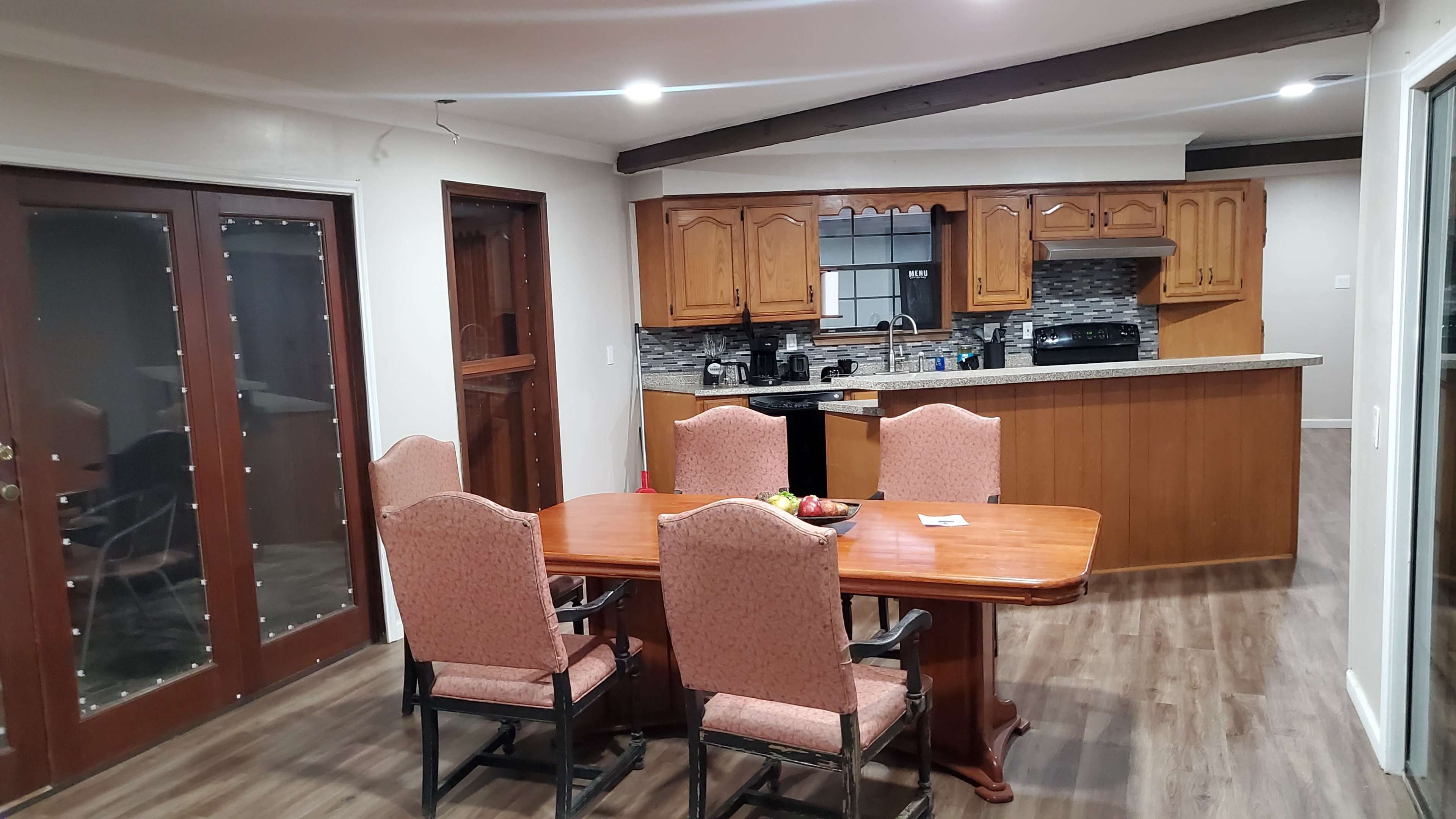 A dining area with a wooden table and chairs, adjacent to a kitchen featuring wooden cabinets and modern appliances.