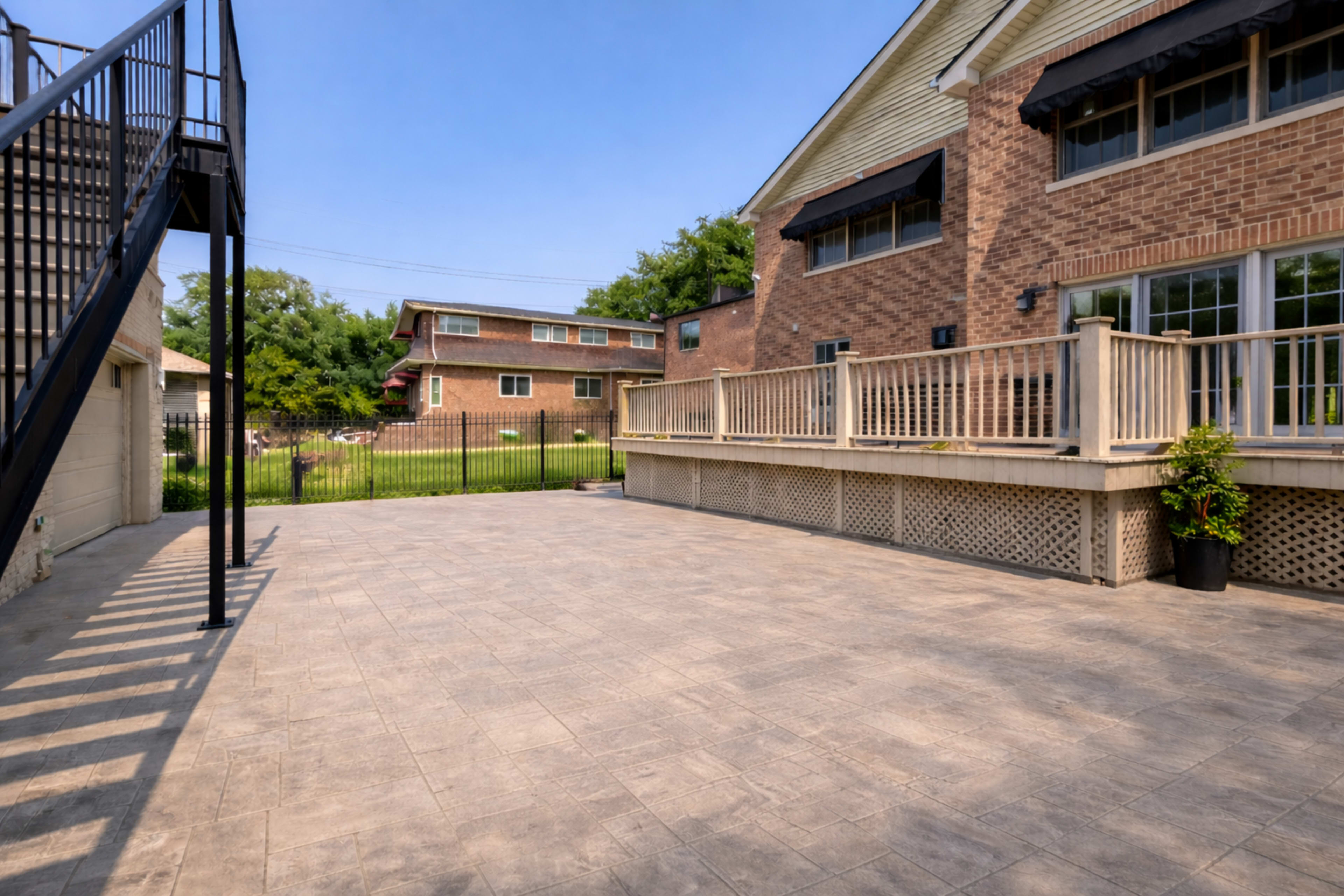 The image shows a paved outdoor patio area adjacent to a two-story brick building with a wooden deck and a spiral staircase leading to the upper level.