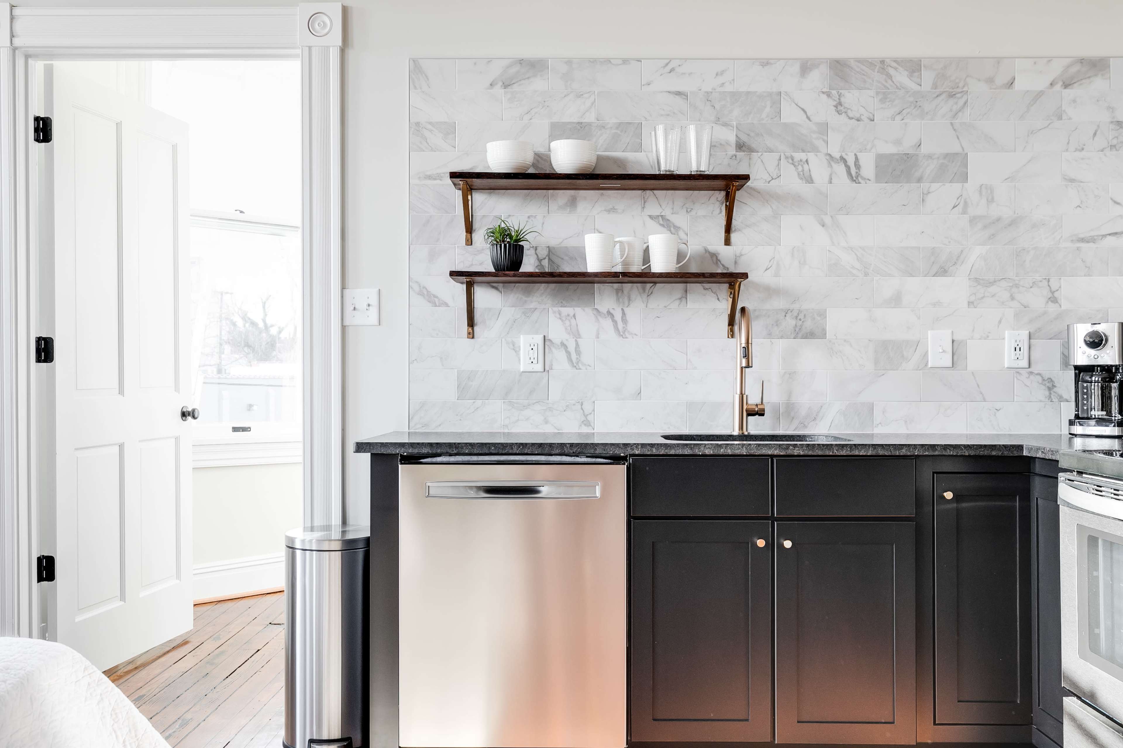 A modern kitchen featuring a marble backsplash, dark cabinetry, and open shelving displaying kitchenware.