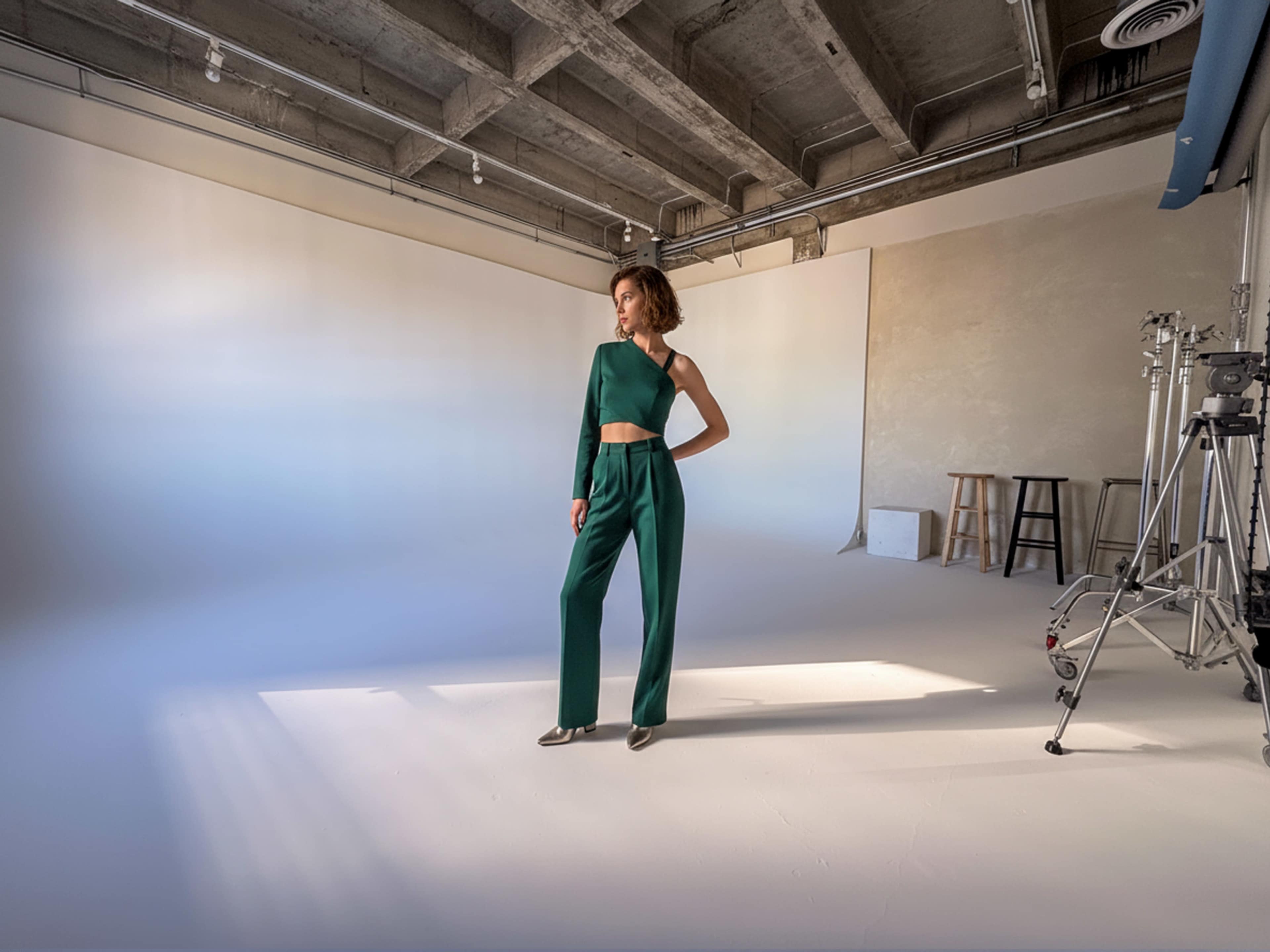 A model poses in a green two-piece outfit in a well-lit photography studio with a neutral background.