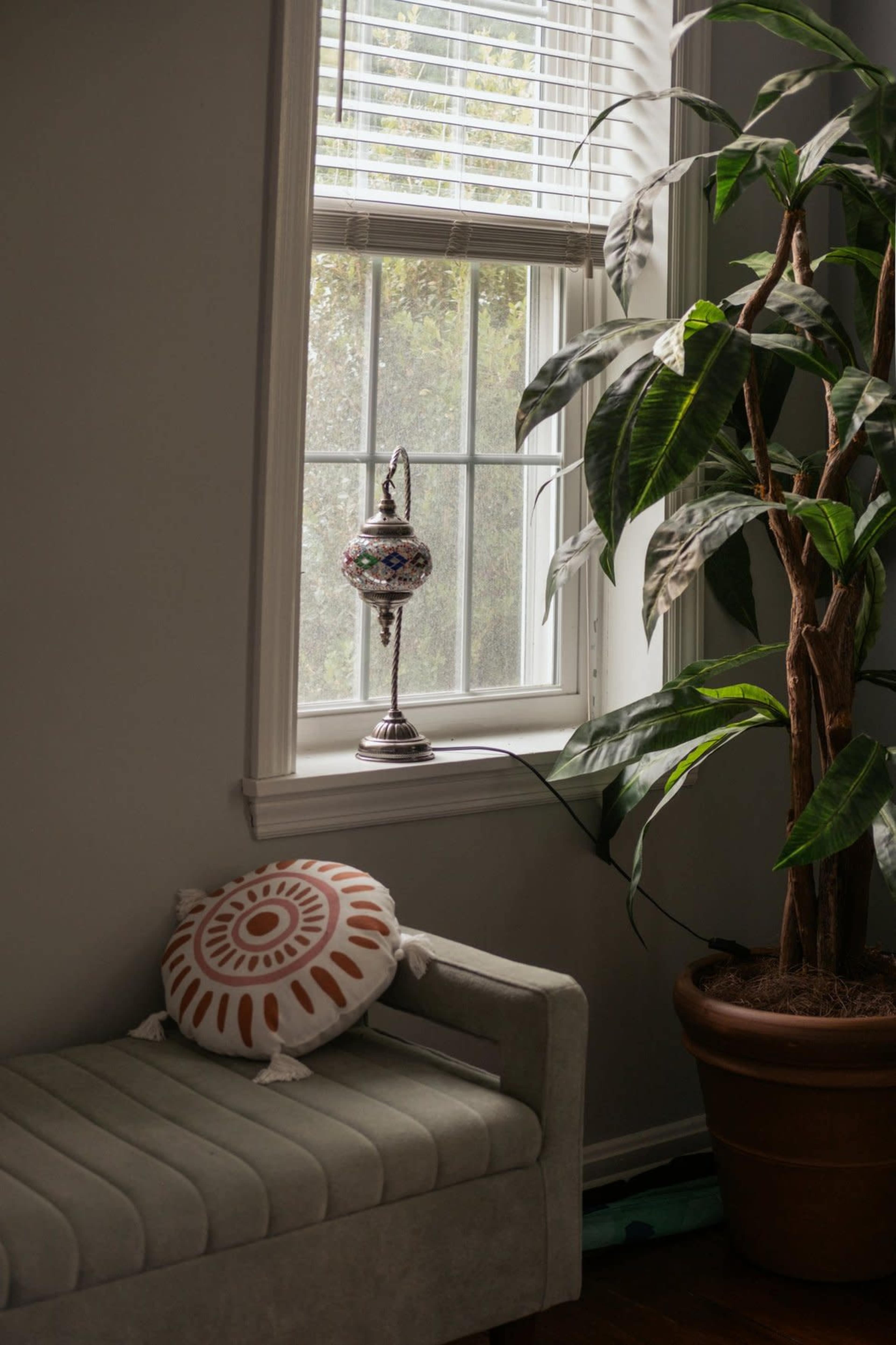 A patterned lamp stands on a windowsill next to a potted plant, with a sofa nearby.