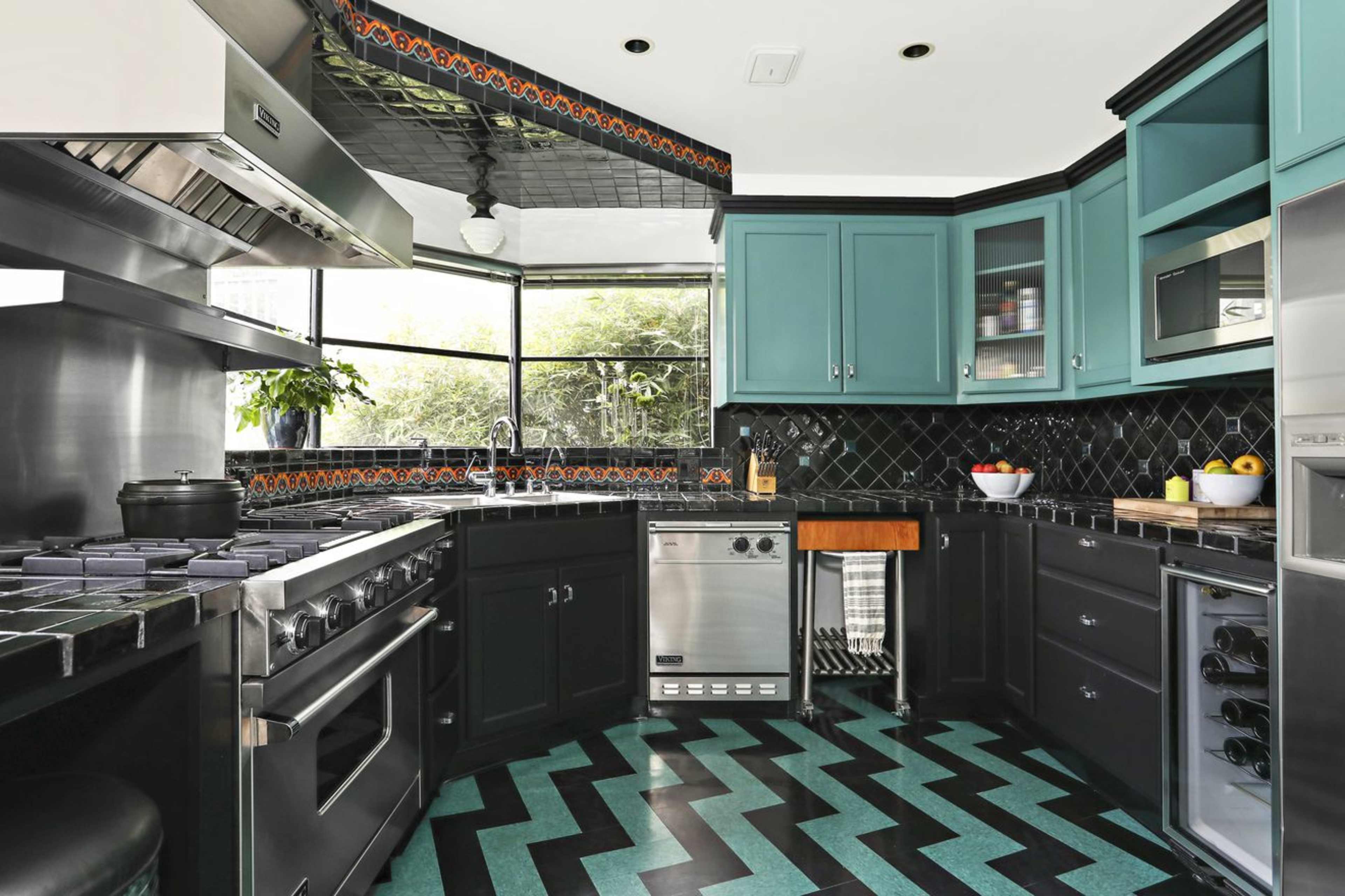 The kitchen features black and teal cabinetry, a stainless steel refrigerator, a gas stove, and a zigzag patterned floor.