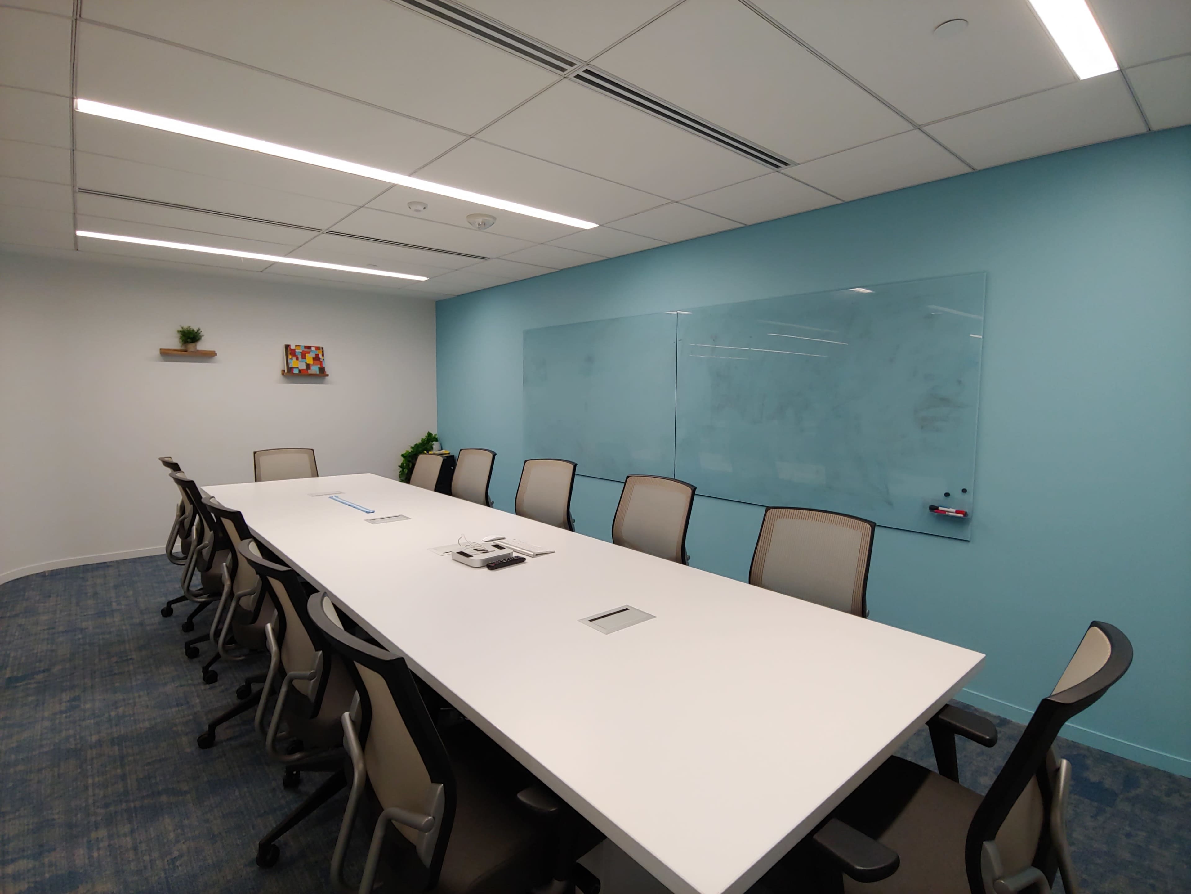 A modern conference room with a long white table, ergonomic chairs, and a blue accent wall featuring a clear whiteboard.