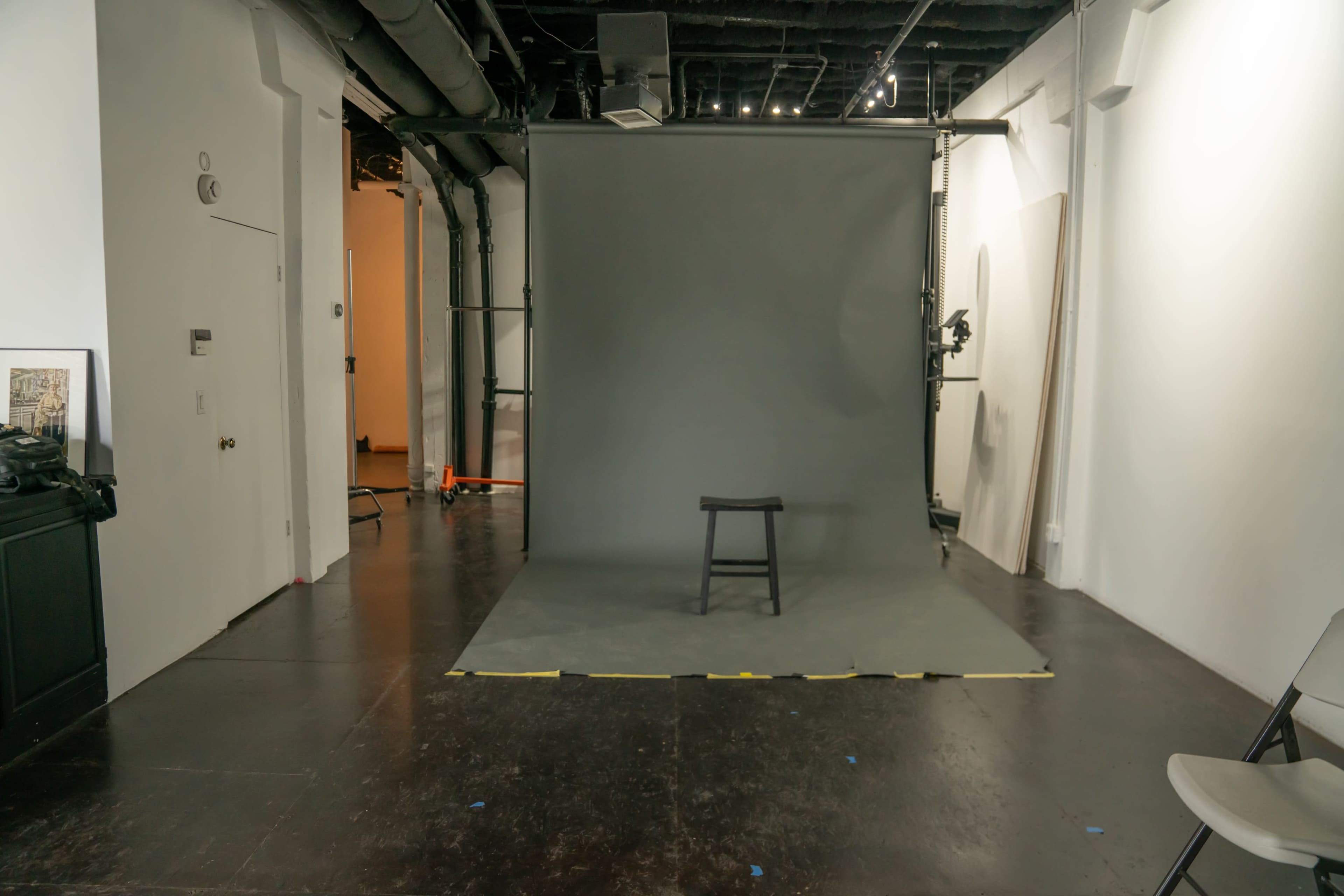A minimalist photography studio featuring a gray backdrop, a wooden stool, and minimal furniture with a polished floor.