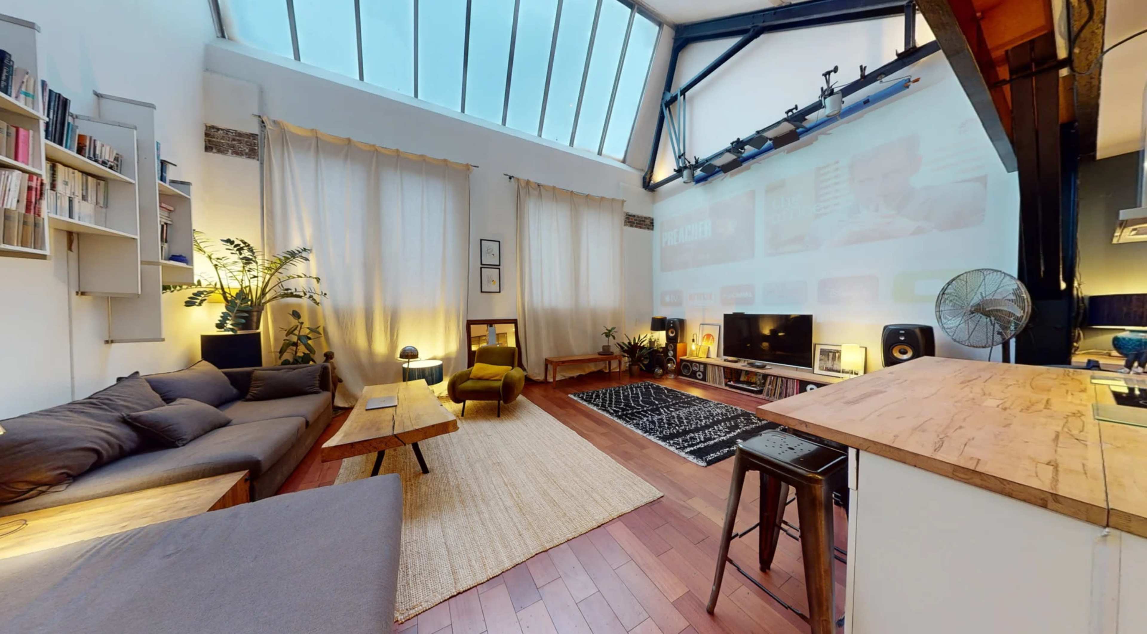 A modern living room with large windows, a comfortable sofa, a wooden table, and a projector displaying content on a wall.