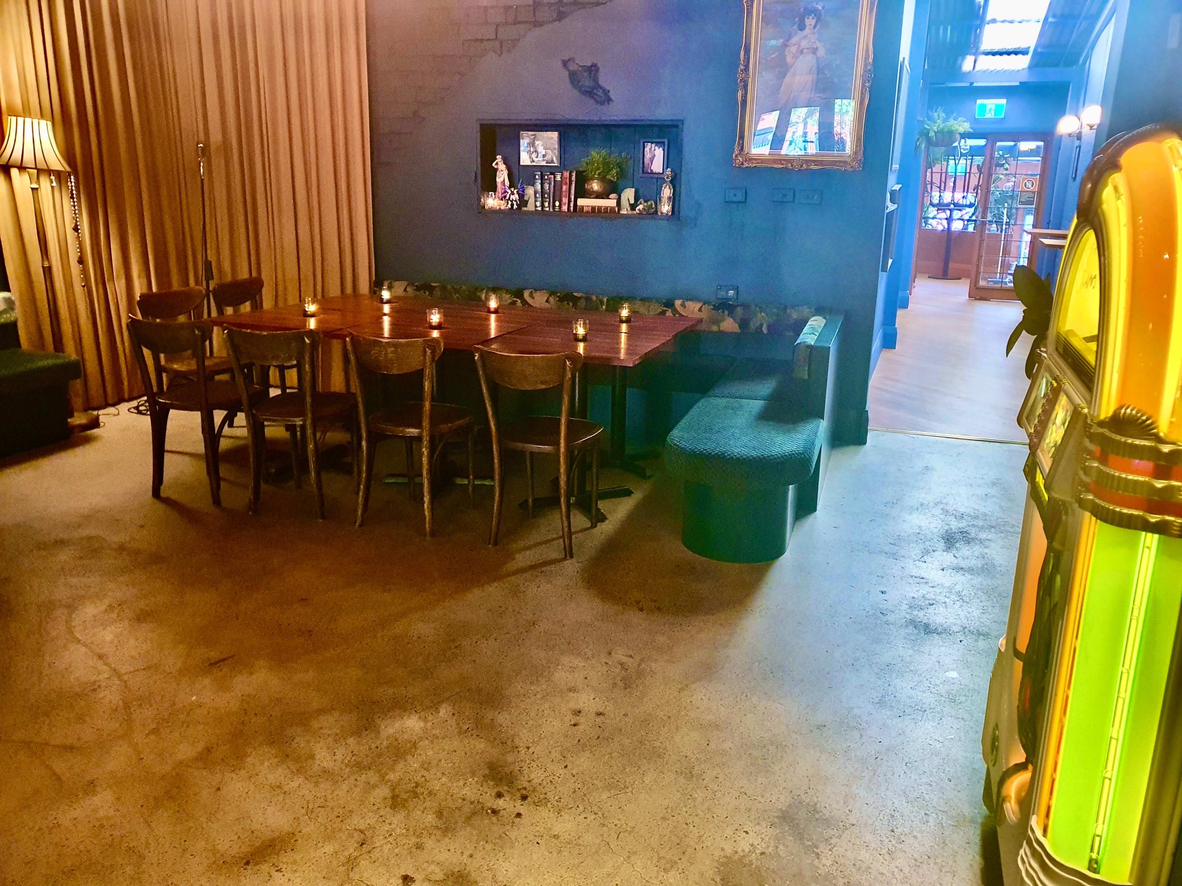 A spacious interior features a large wooden dining table surrounded by chairs, a jukebox in the corner, and textured walls adorned with decor.
