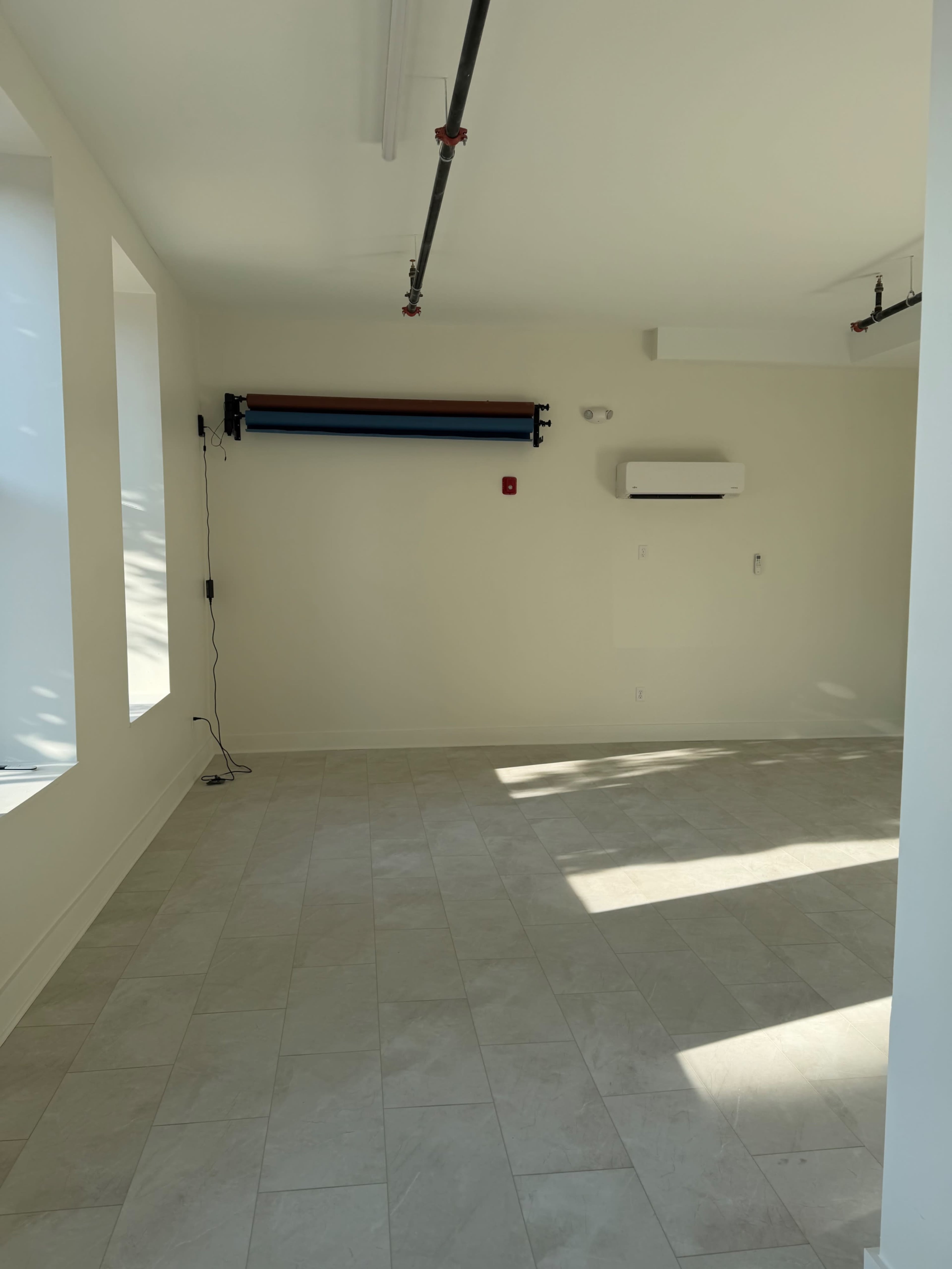 The image shows an empty room with light-colored walls, a light tile floor, and a roll of backdrop paper mounted on the wall.
